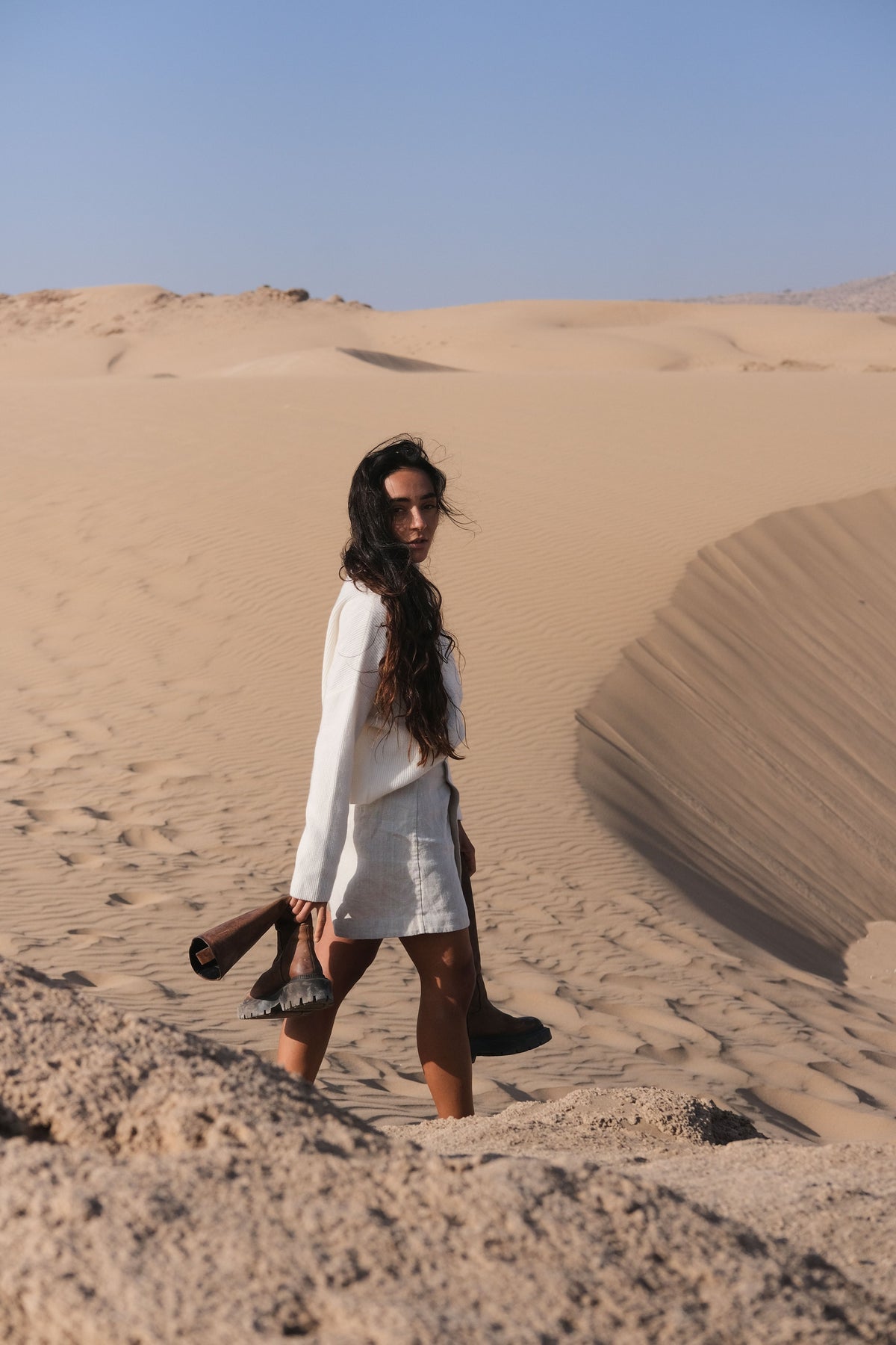 LILLY PILLY Lumi cashmere knit in Ivory walking in a desert landscape with sand dunes and clear sky.