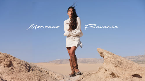 LILLY PILLY woman in a ivory white Lumi cashmere knit paired with Betty linen skirt and brown boots standing on desert rocks