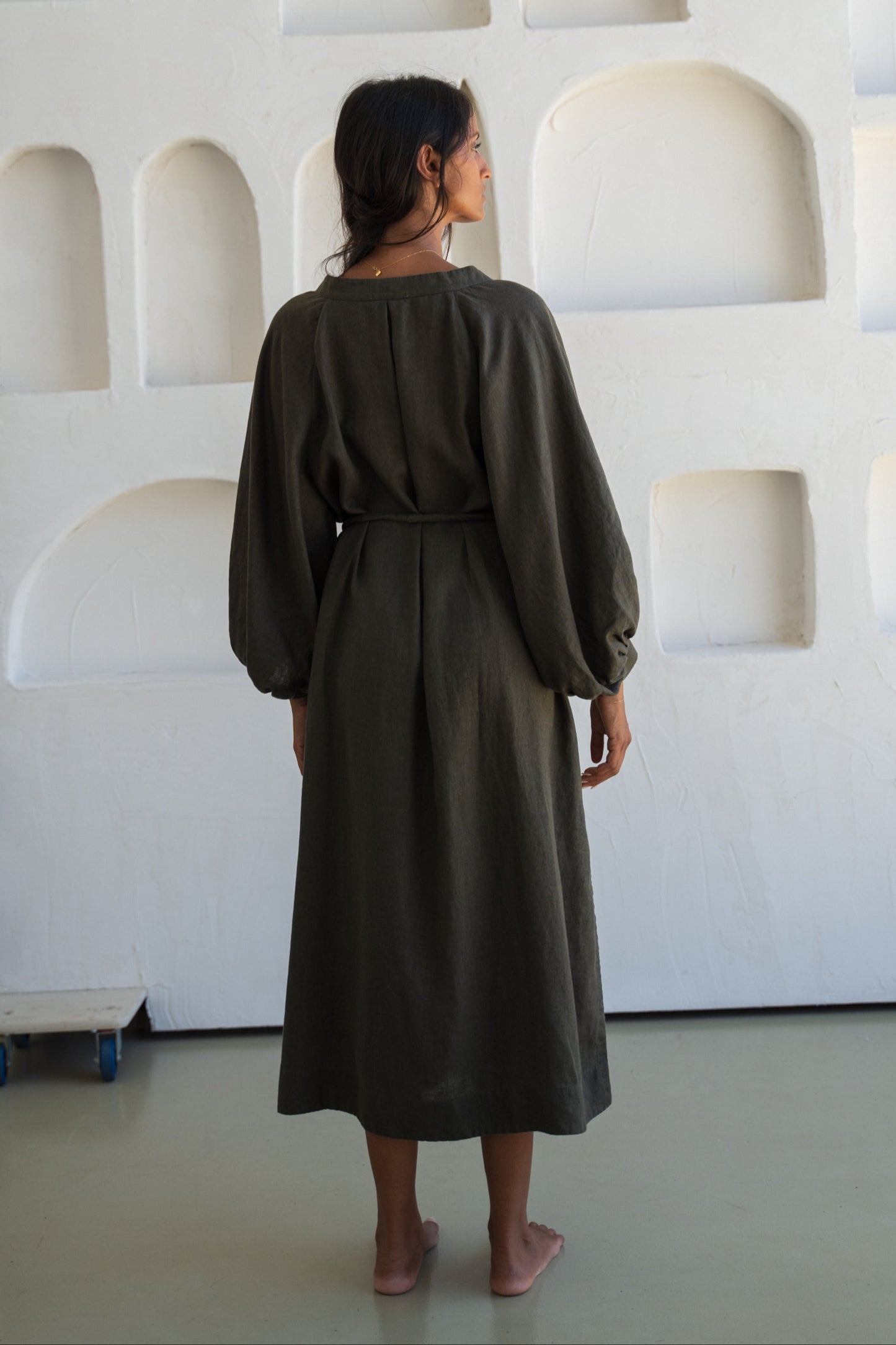 Woman wearing a khaki Mae linen dress in studio, back view