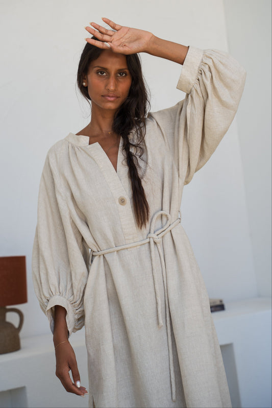 Woman wearing a Mae oatmeal linen dress close up view in a room with white walls and a mirror.