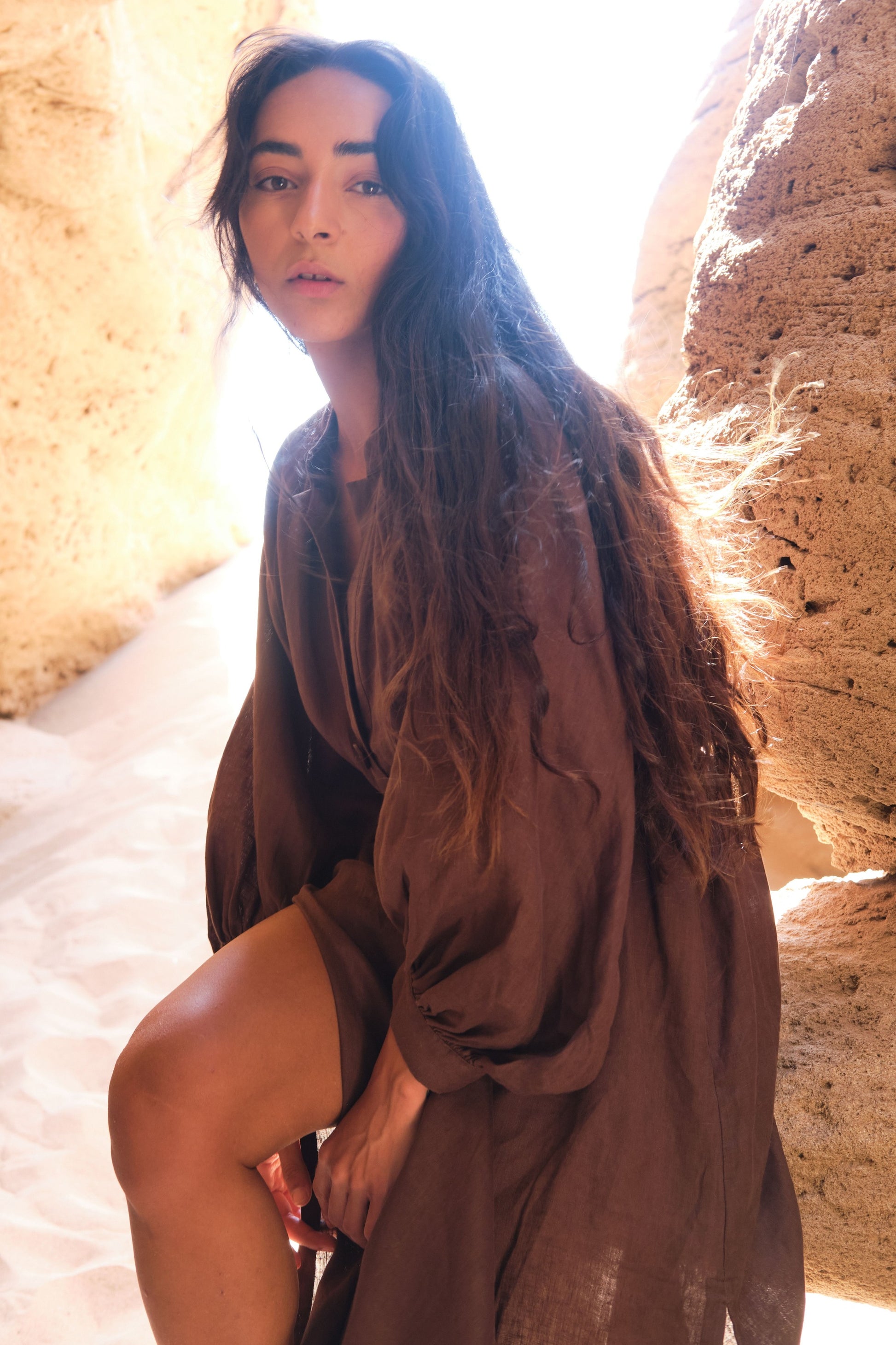 LILLY PILLY woman wearing a chocolate brown Mae linen dress standing in a sunlit stone passageway