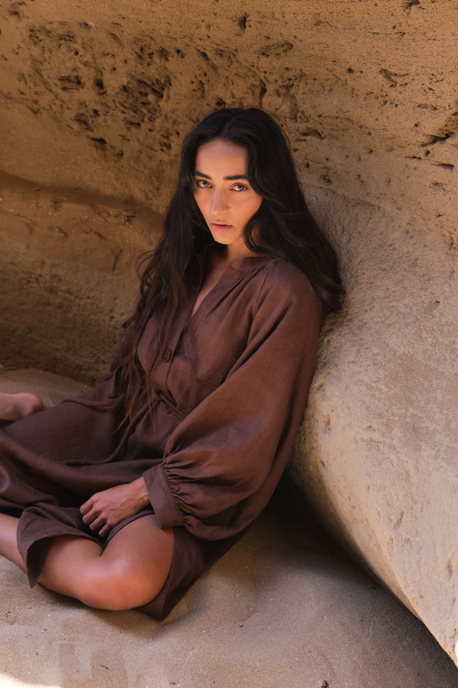 LILLY PILLY woman wearing a chocolate brown Mae linen dress sitting in a stone alcove