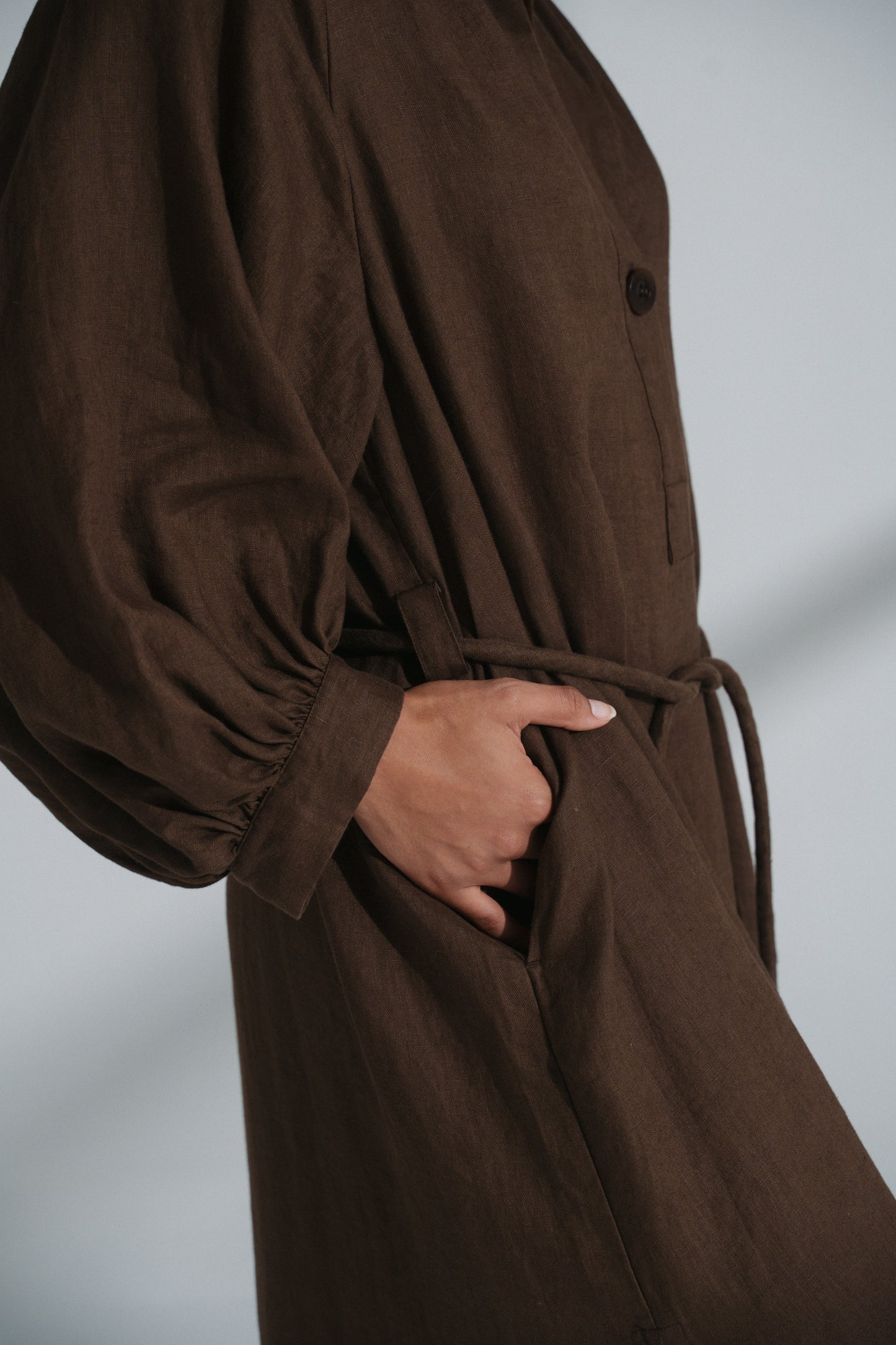 LILLY PILLY woman wearing a chocolate brown Mae linen dress while holding their hand in the pocket against a plain background