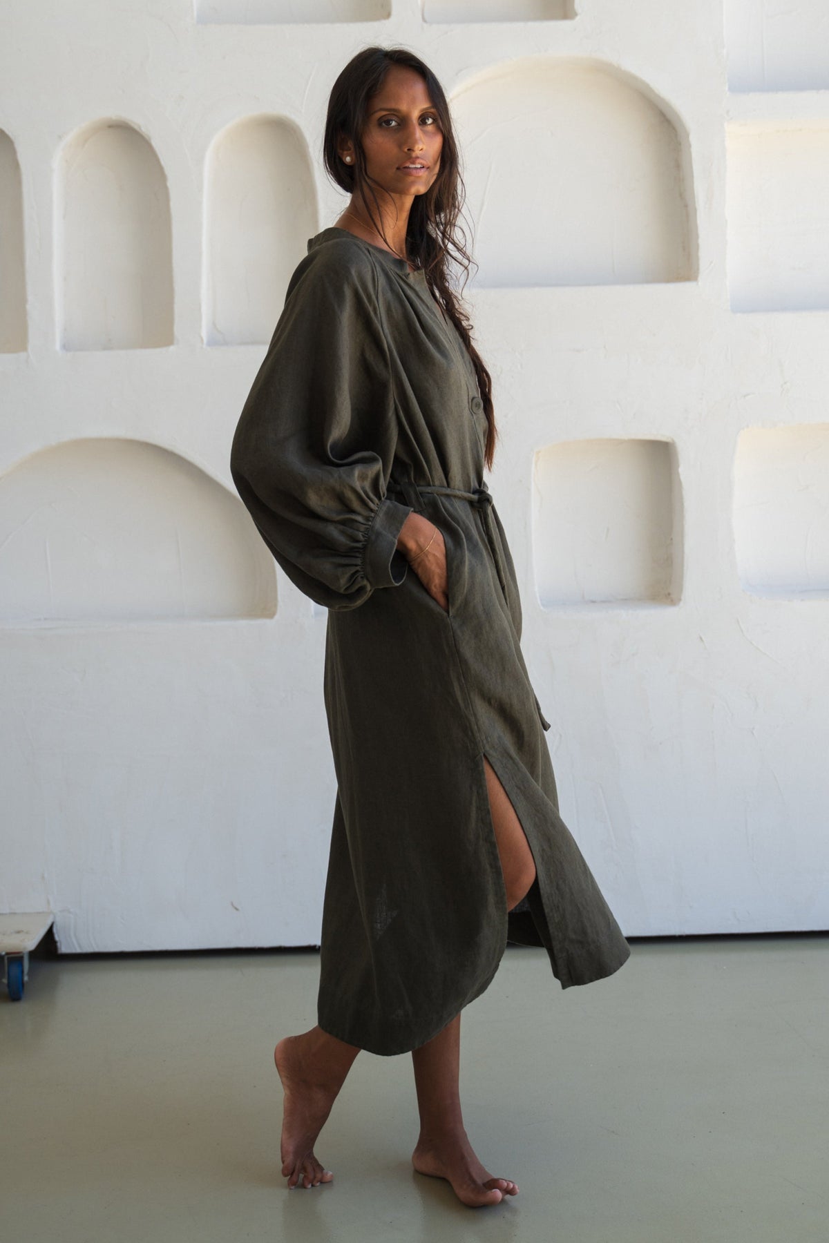 Woman wearing a khaki Mae linen dress in studio side view