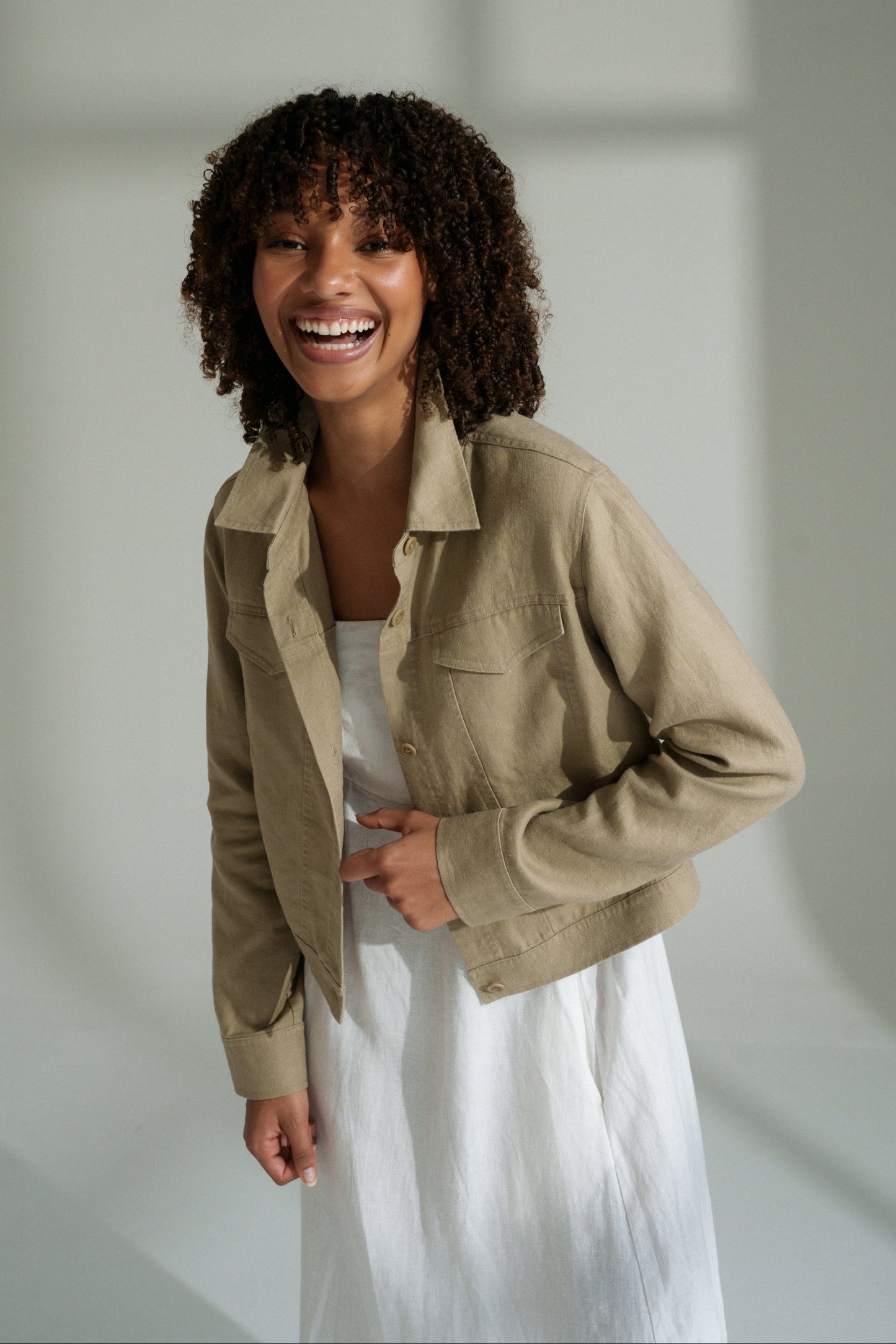 LILLY PILLY woman wearing a taupe Milly linen jacket over a white dress, standing against a plain background