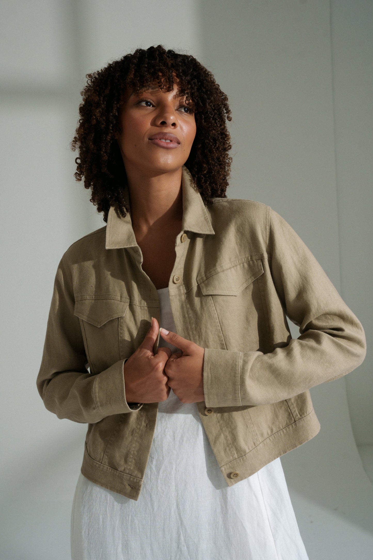 LILLY PILLY woman wearing a taupe Milly linen jacket over a white dress against a plain background