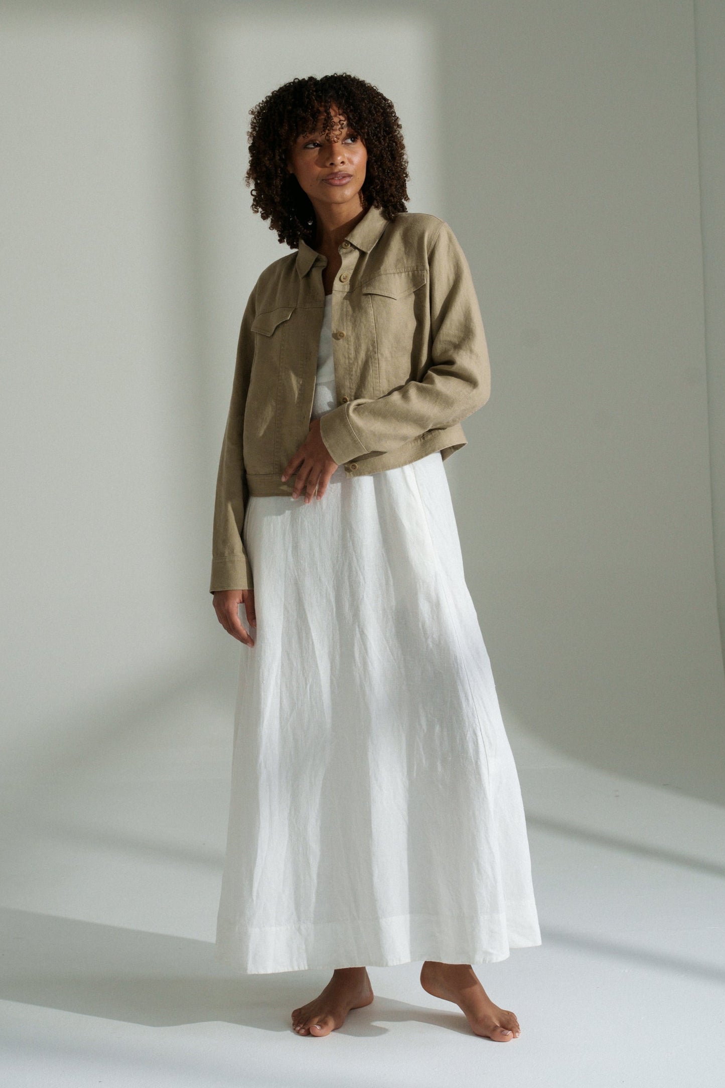 LILLY PILLY woman wearing a taupe Milly linen jacket and white skirt standing against a plain white background