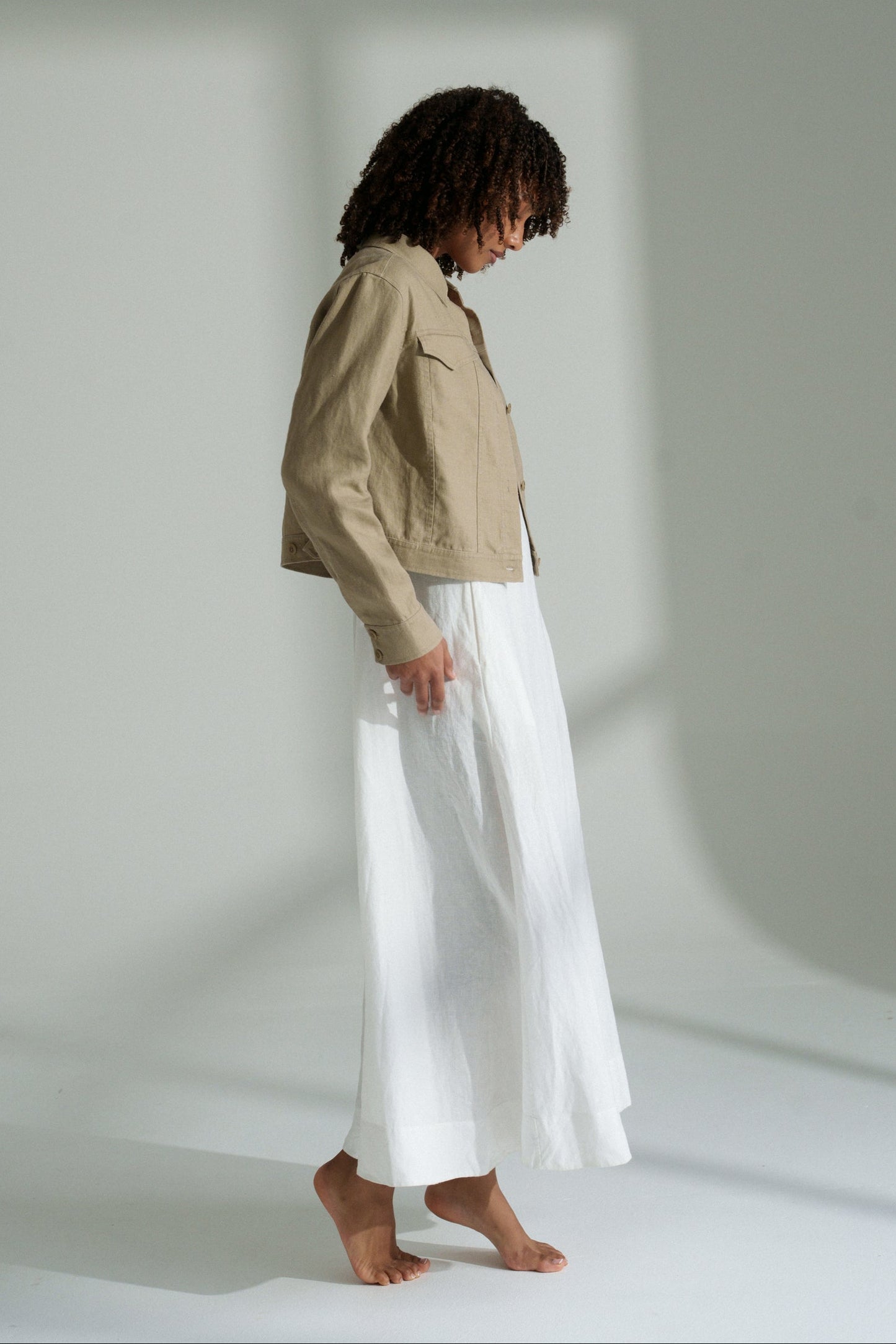 LILLY PILLY woman wearing a taupe Milly linen jacket and white pants standing against a plain background