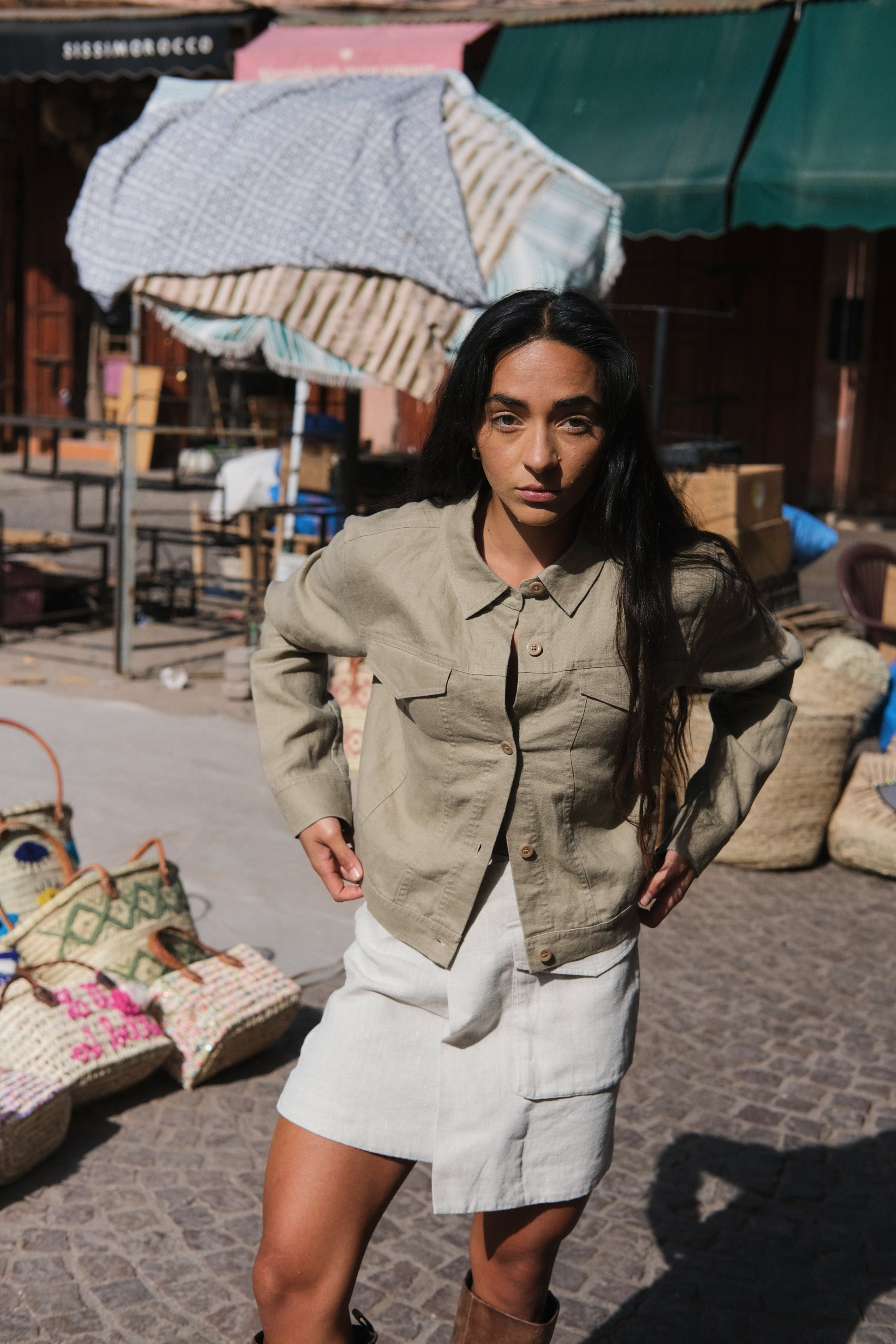 LILLY PILLY woman wearing a taupe Milly linen jacket standing outdoors with a market scene in the background