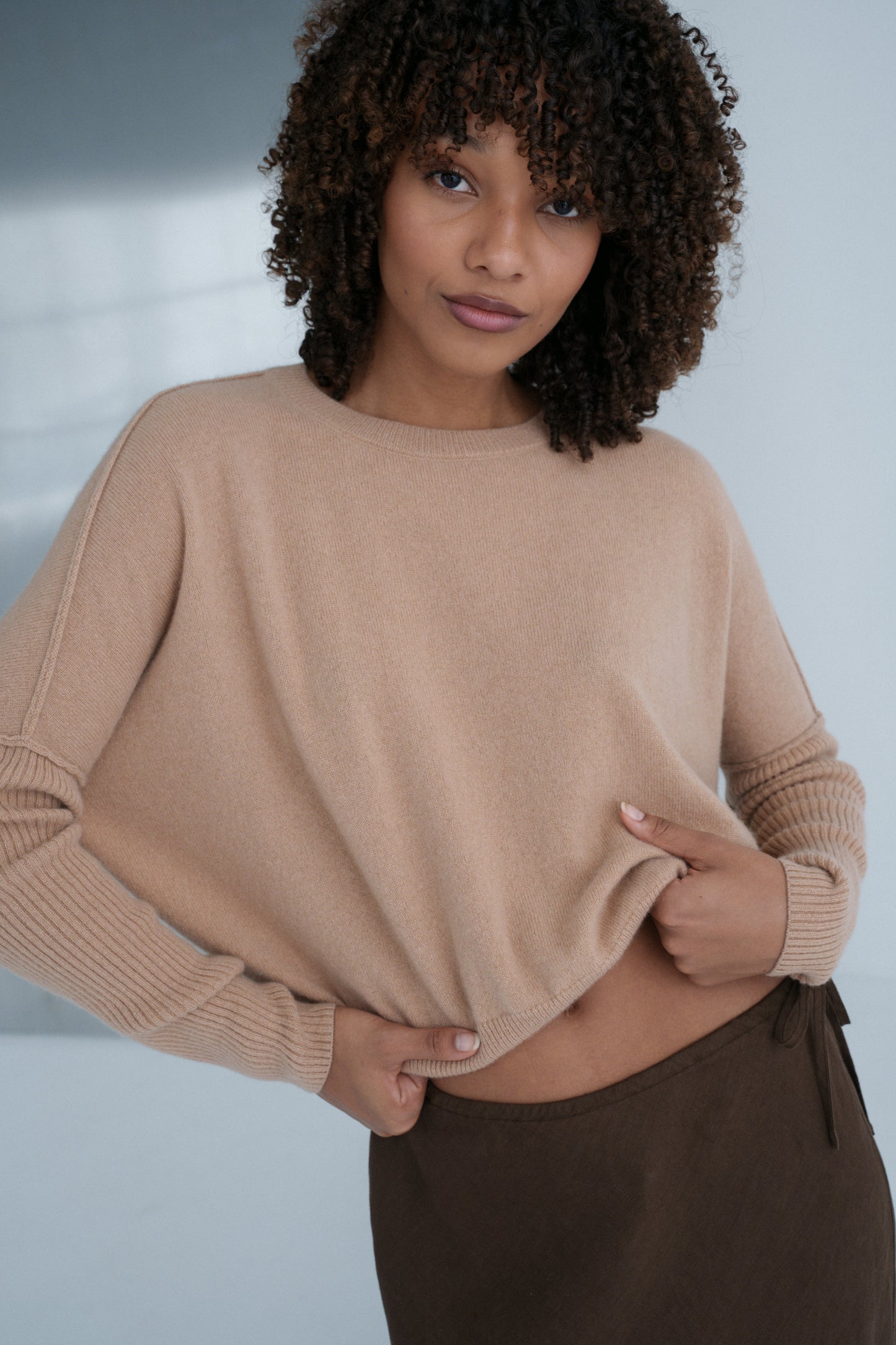 Close up of LILLY PILLY woman wearing Miri cashmere knit sweater in Camel brown against a plain background