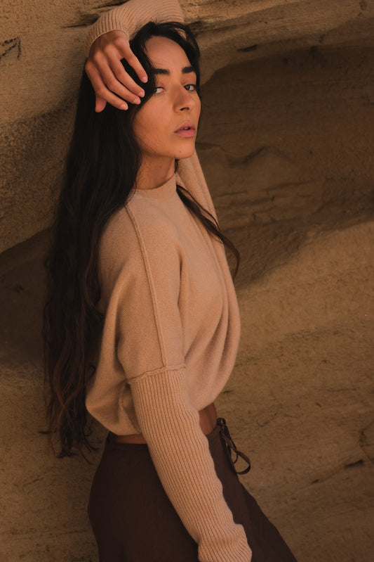 LILLY PILLY woman wearing Camel brown Miri cashmere knit sweater  standing against a textured wall