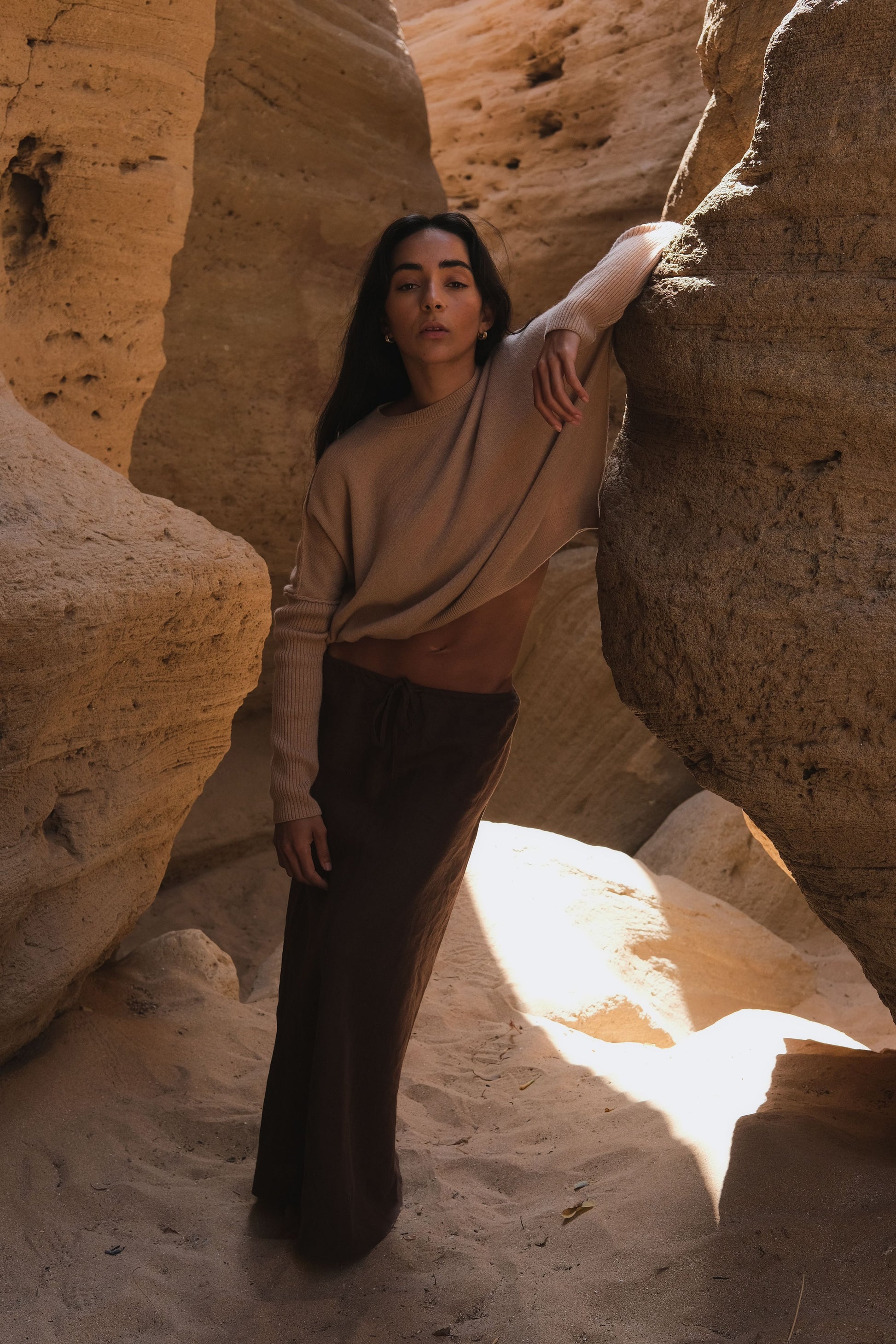 LILLY PILLY woman wearing Camel brown Miri cashmere knit sweater  standing in a natural rock formation with sunlight filtering through