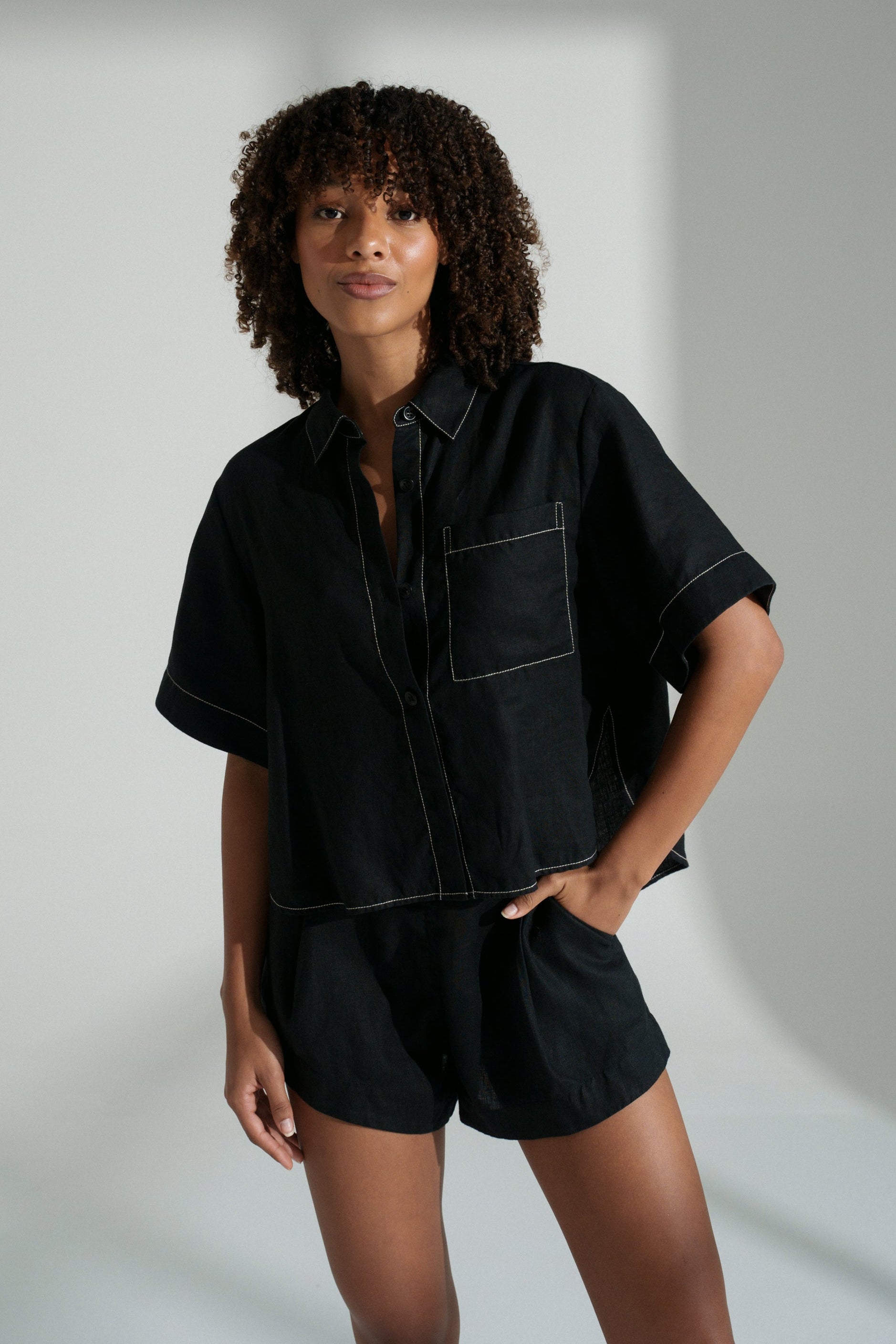 LILLY PILLY woman wearing a black Nika linen shirt top and Gaia linen shorts outfit against a neutral background