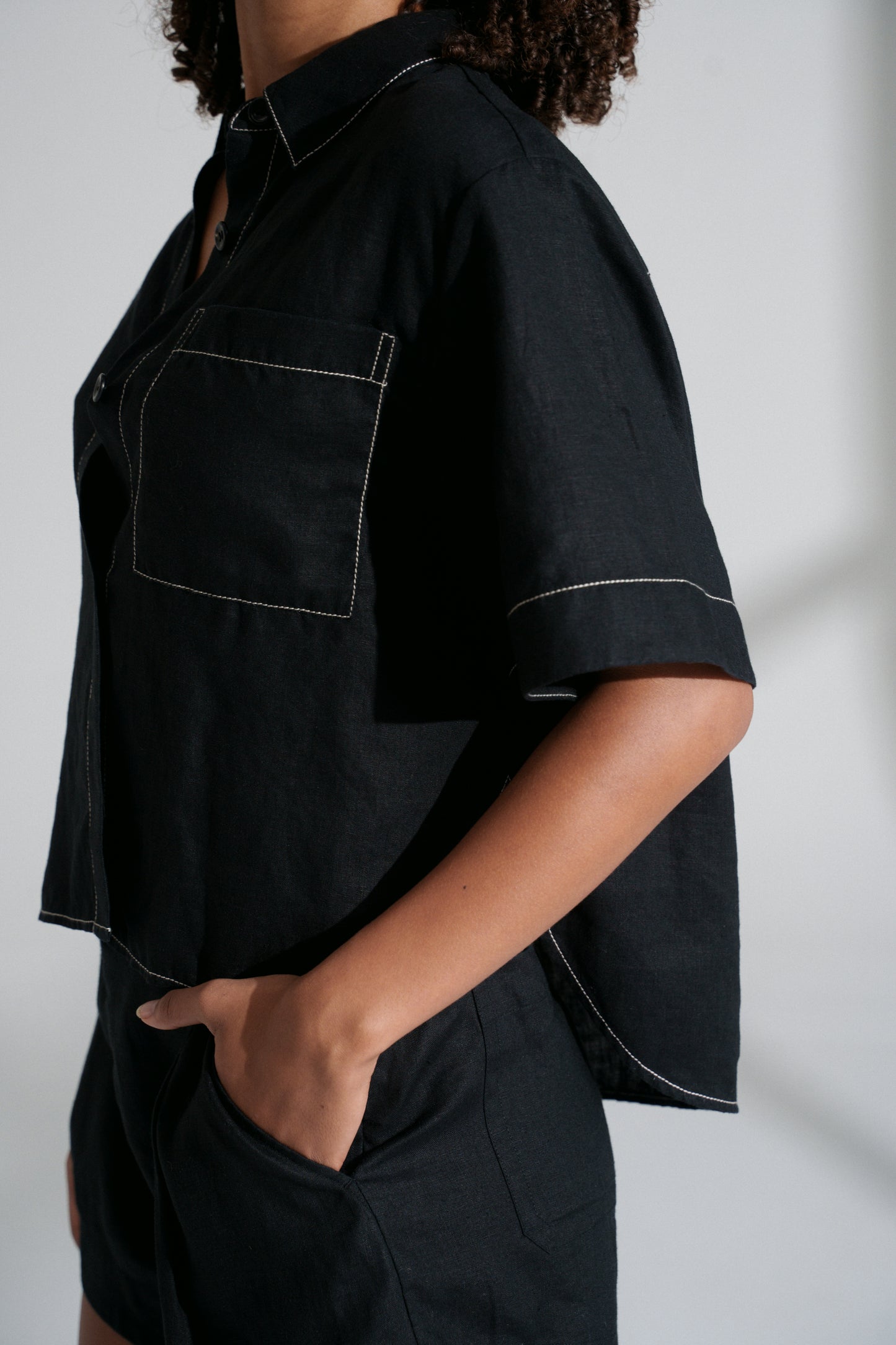 LILLY PILLY woman wearing a black Nika linen shirt top and Gaia linen shorts outfit against a neutral background showing close up view of pocket detail