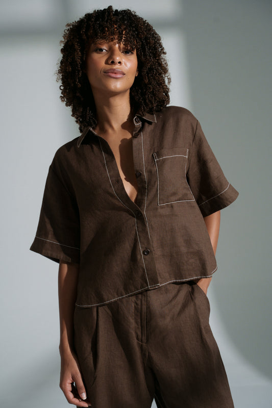 LILLY PILLY woman wearing a chocolate Nika linen shirt top against a gray background