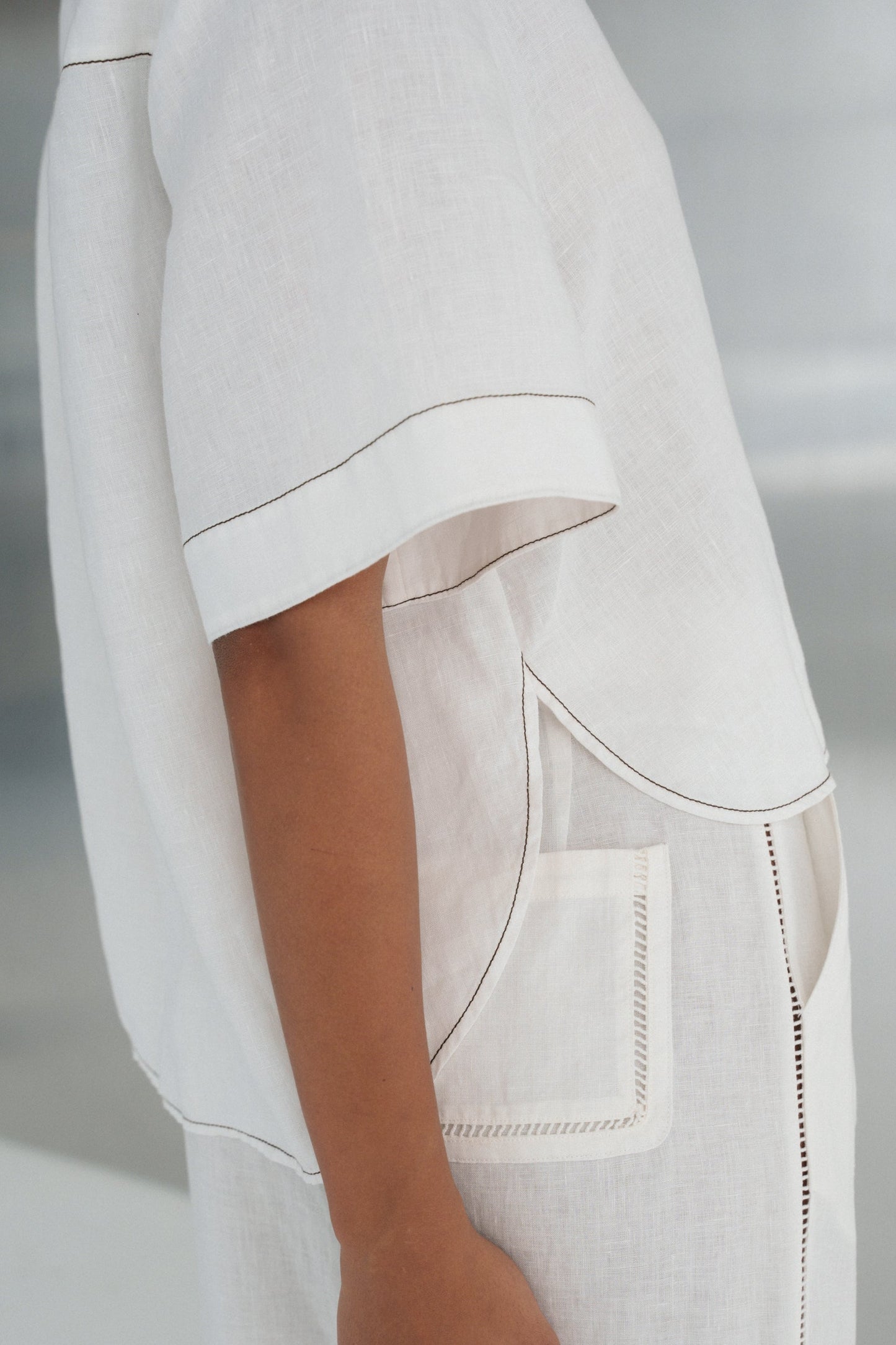 Close up, side view of LILLY PILLY woman wearing an ivory Nika linen shirt top and Ivy linen pants outfit with a pocket on a neutral background