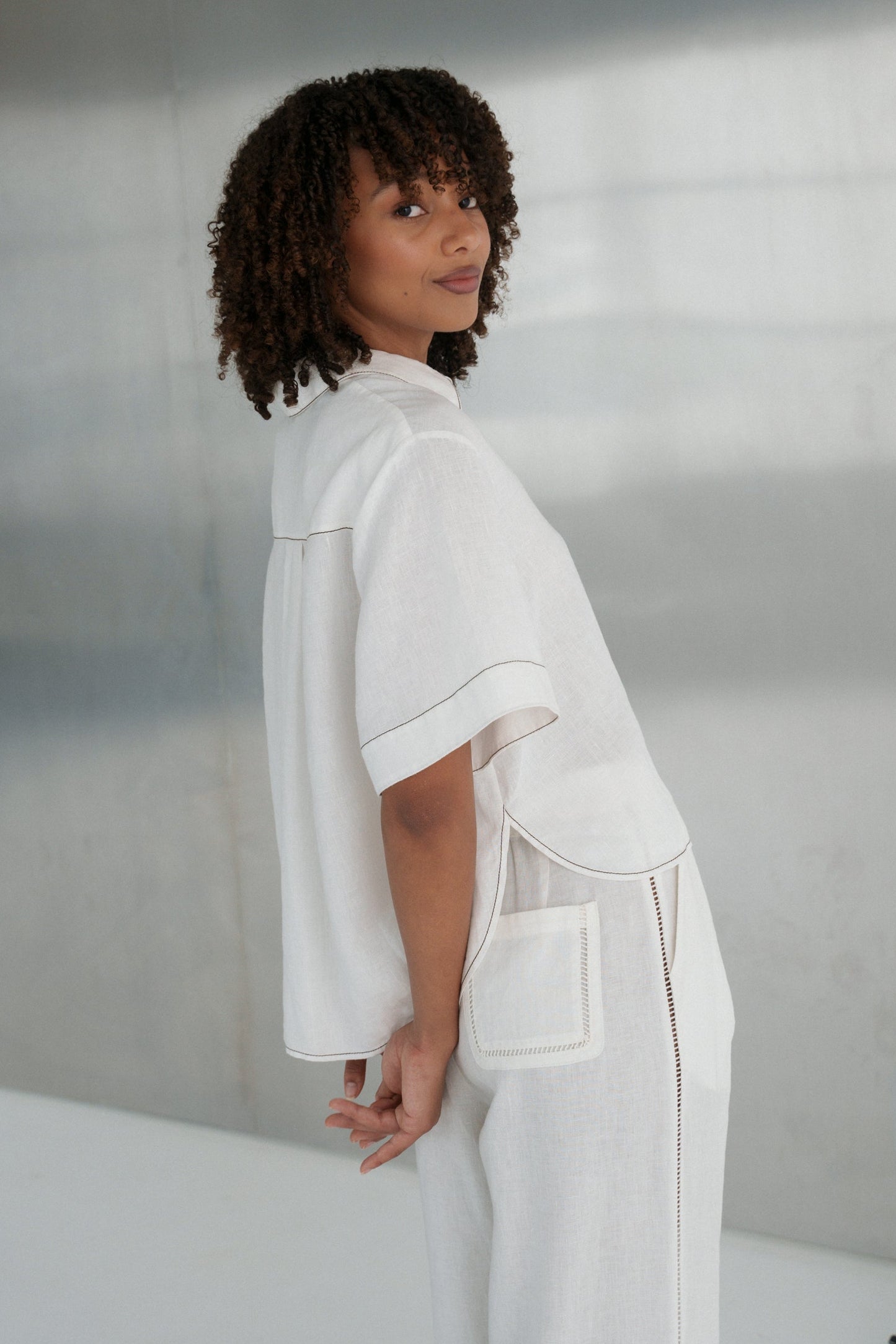LILLY PILLY woman wearing an ivory Nika linen shirt top and Ivy linen pants outfit in a minimalistic setting