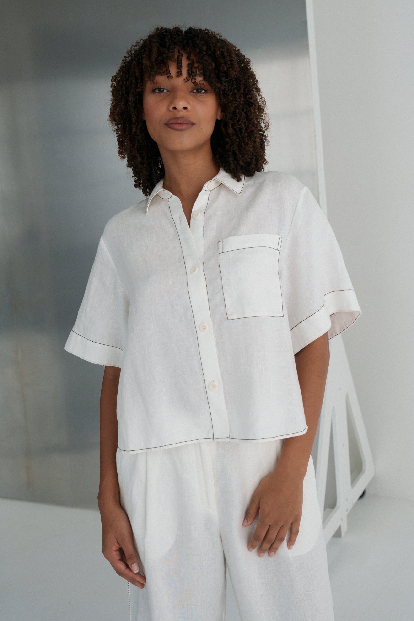 LILLY PILLY woman wearing an ivory Nika linen shirt top and Ivy linen pants outfit standing against a neutral background