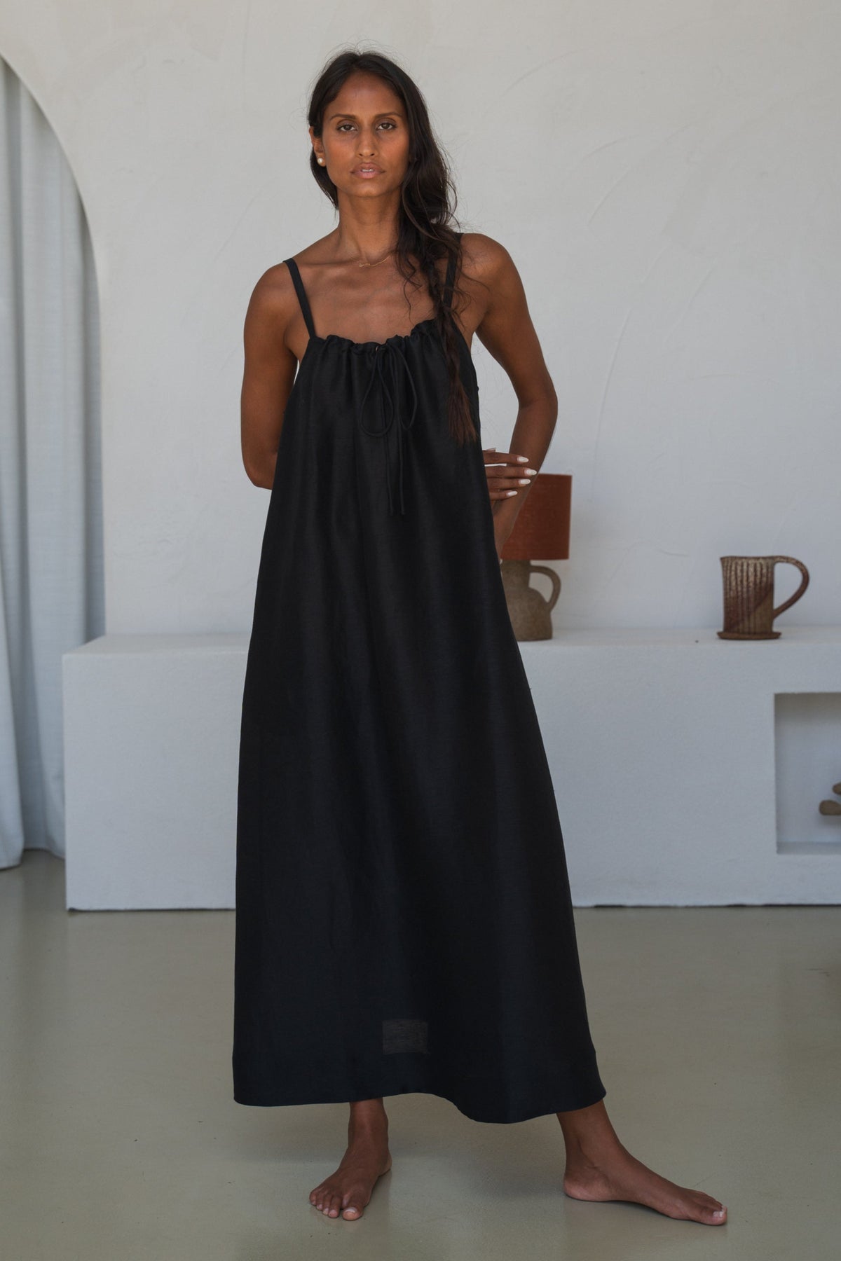 Woman wearing a black dress standing in a minimalistic room with white walls and a white floor.