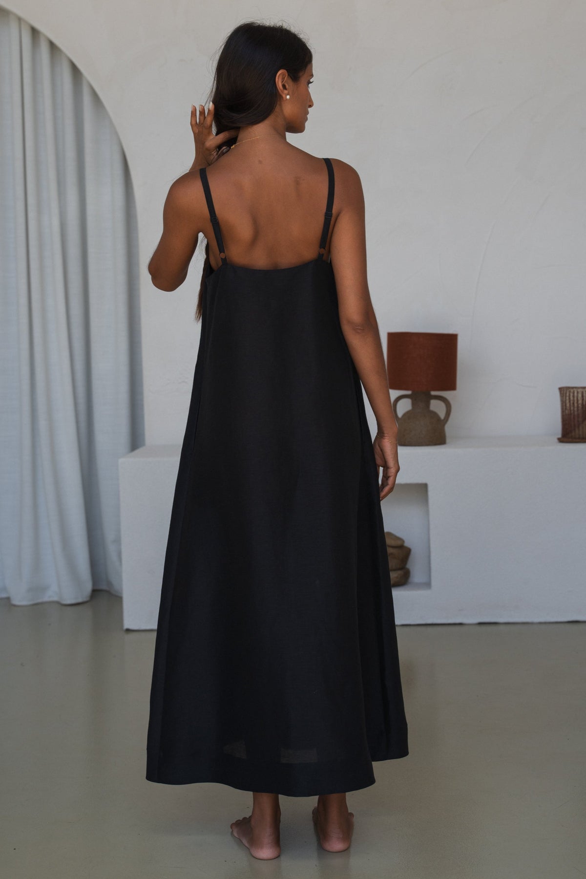 Back view of woman wearing a black slip dress in a minimal indoor setting