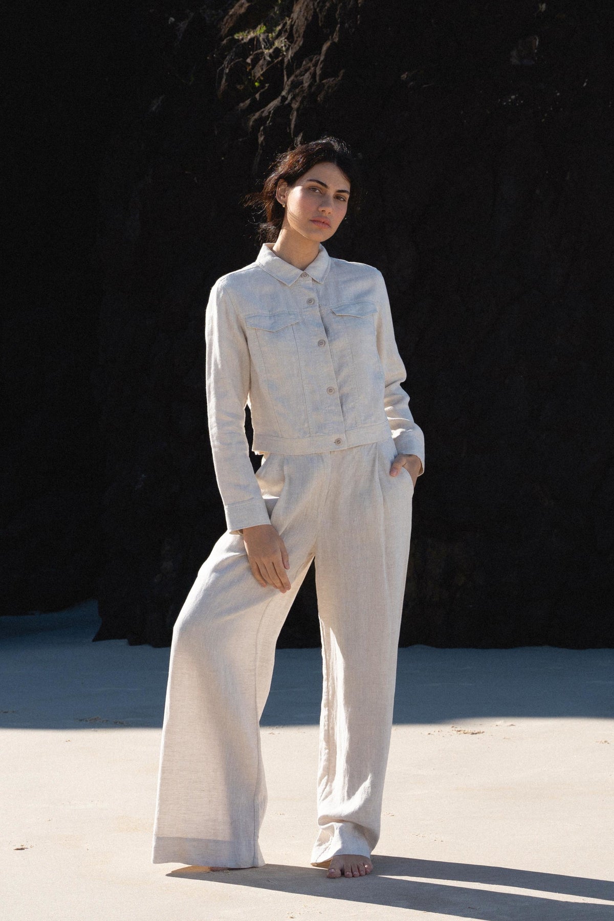 LILLY PILLY woman wearing a Milly linen jacket and Oli linen pants in oatmeal standing against a dark background