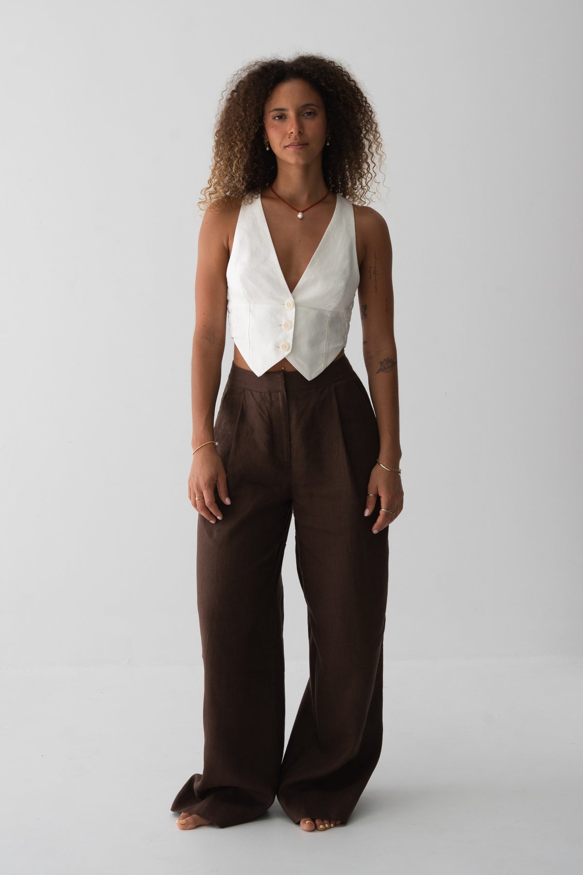 Oli Linen Pants in Chocolate - full length front view, woman wearing Chocolate wide-leg linen pants with ivory V-neck linen waistcoat, studio backdrop - Lilly Pilly Collection