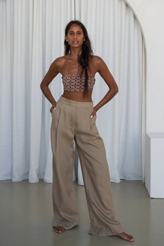 Oli Linen Pants in Taupe - full length front view, woman wearing Taupe wide-leg linen pants with printed bandeau top, hands in pockets, white curtain backdrop - Lilly Pilly Collection