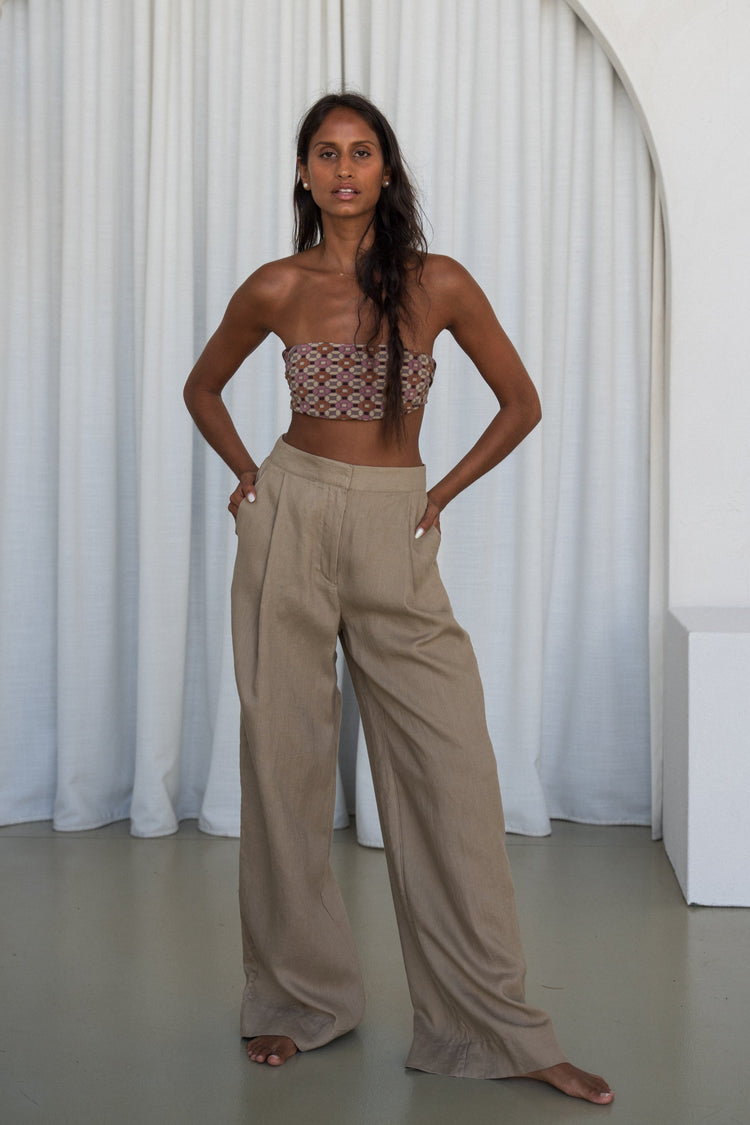 Oli Linen Pants in Taupe - full length front view, woman wearing Taupe wide-leg linen pants with printed bandeau top, hands in pockets, white curtain backdrop - Lilly Pilly Collection