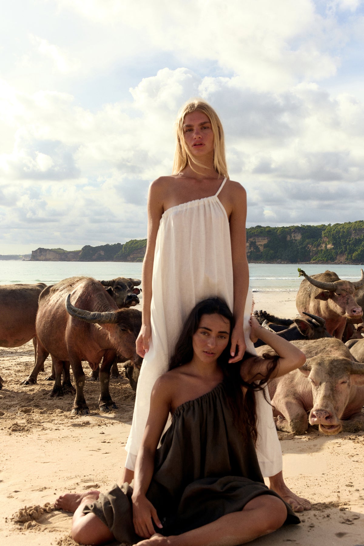 Ophelia Linen Midi Dress in Ivory - two women standing on beach with cattle, full length view, asymmetric neckline - Lilly Pilly Collection