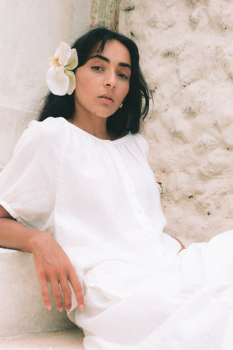 LPia Linen Top in Ivory - woman seated against stone wall, orchid hair detail, gathered neckline and puff sleeves - Lilly Pilly Collection