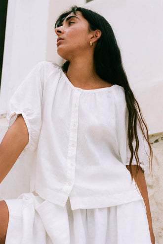 Pia Linen Top in Ivory - three-quarter view, gathered scoop neckline and button-front, whitewashed wall - Lilly Pilly Collection