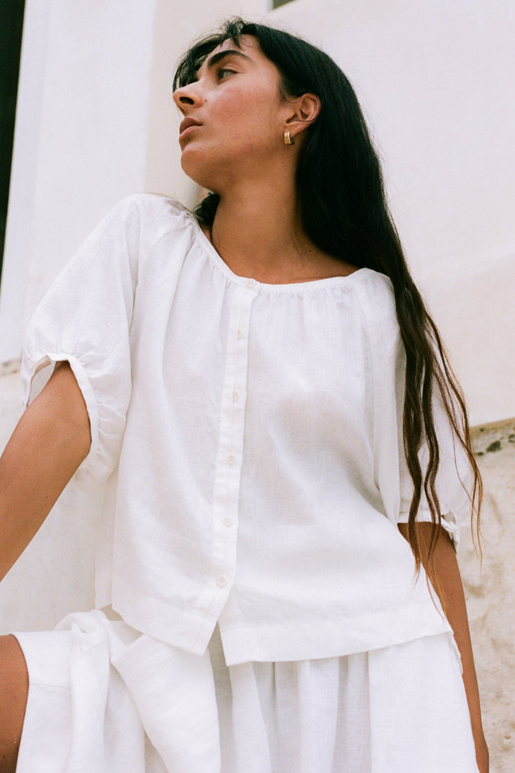 Pia Linen Top in Ivory - three-quarter view, gathered scoop neckline and button-front, whitewashed wall - Lilly Pilly Collection
