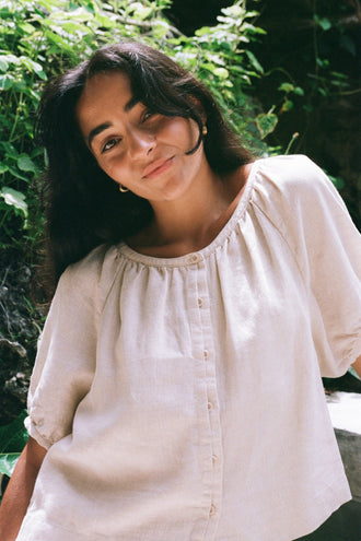 Pia Linen Top in Oatmeal - smiling woman, gathered neckline and puff sleeves, garden setting, styled with Gaia Linen Shorts in Oatmeal - Lilly Pilly Collection