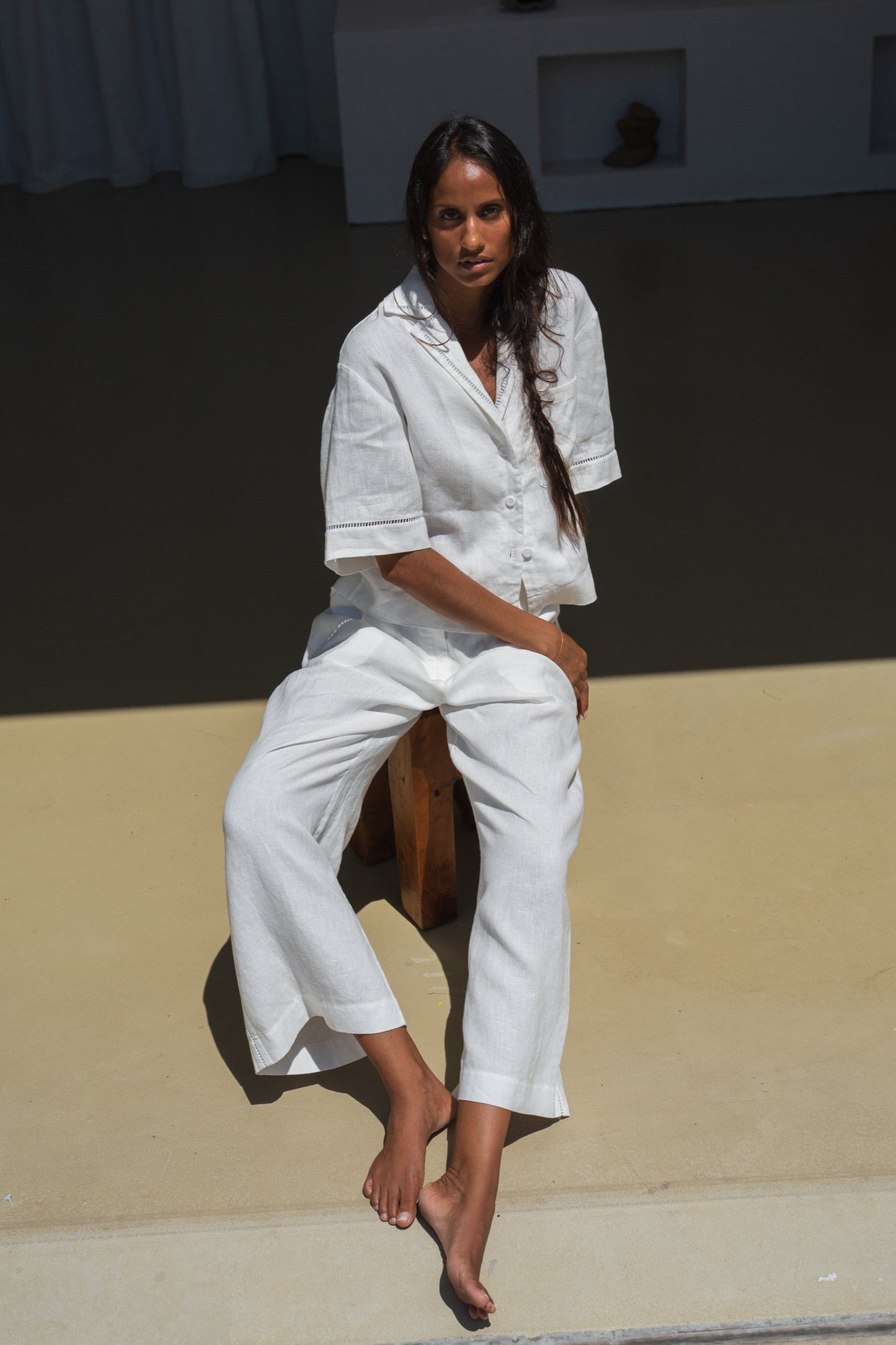 Woman in a ivory Rika linen pants and Quinn shirt sitting on a stool