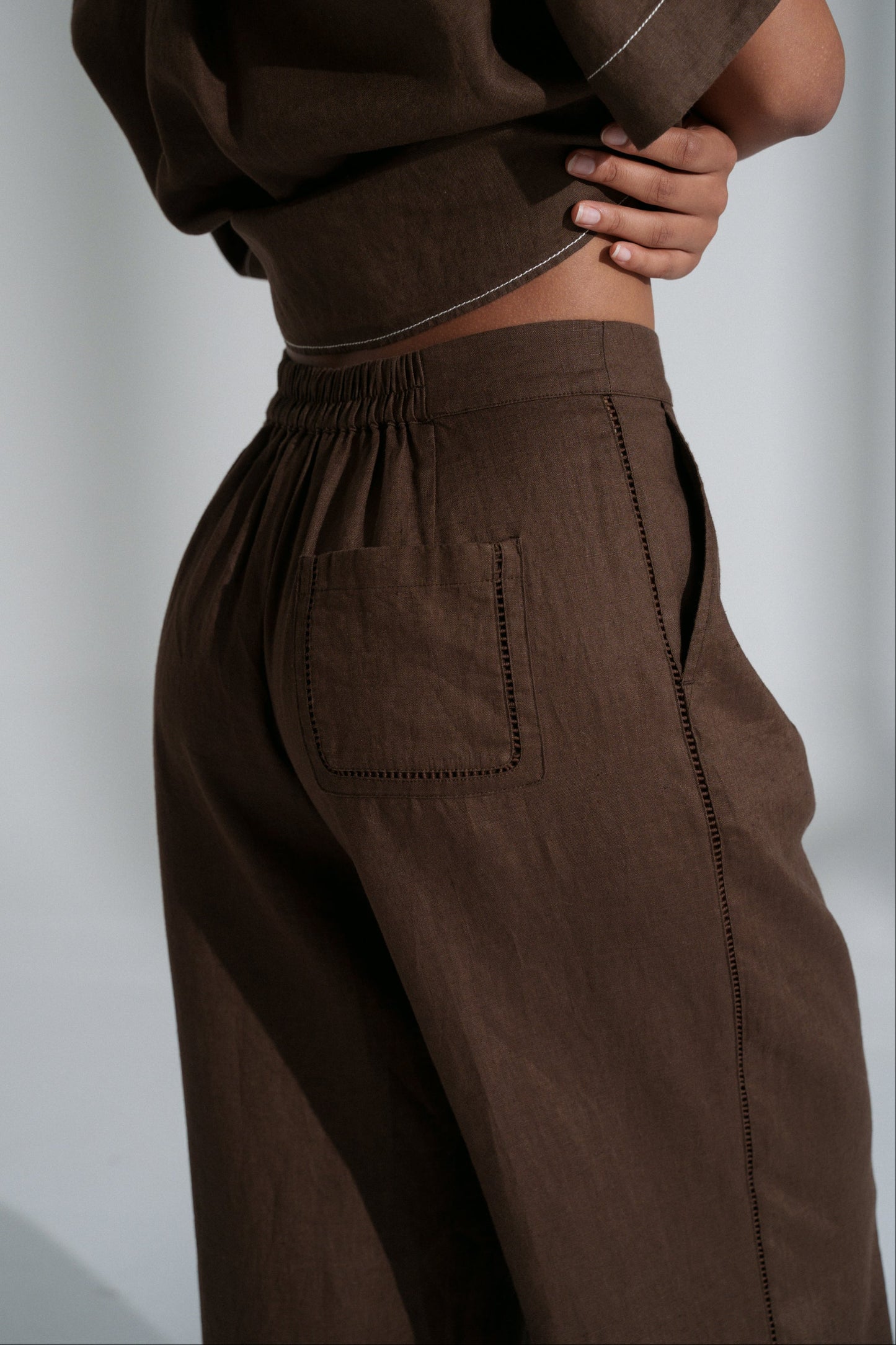 LILLY PILLY woman wearing Rika linen pants in chocolate brown with a plain background, pocket view