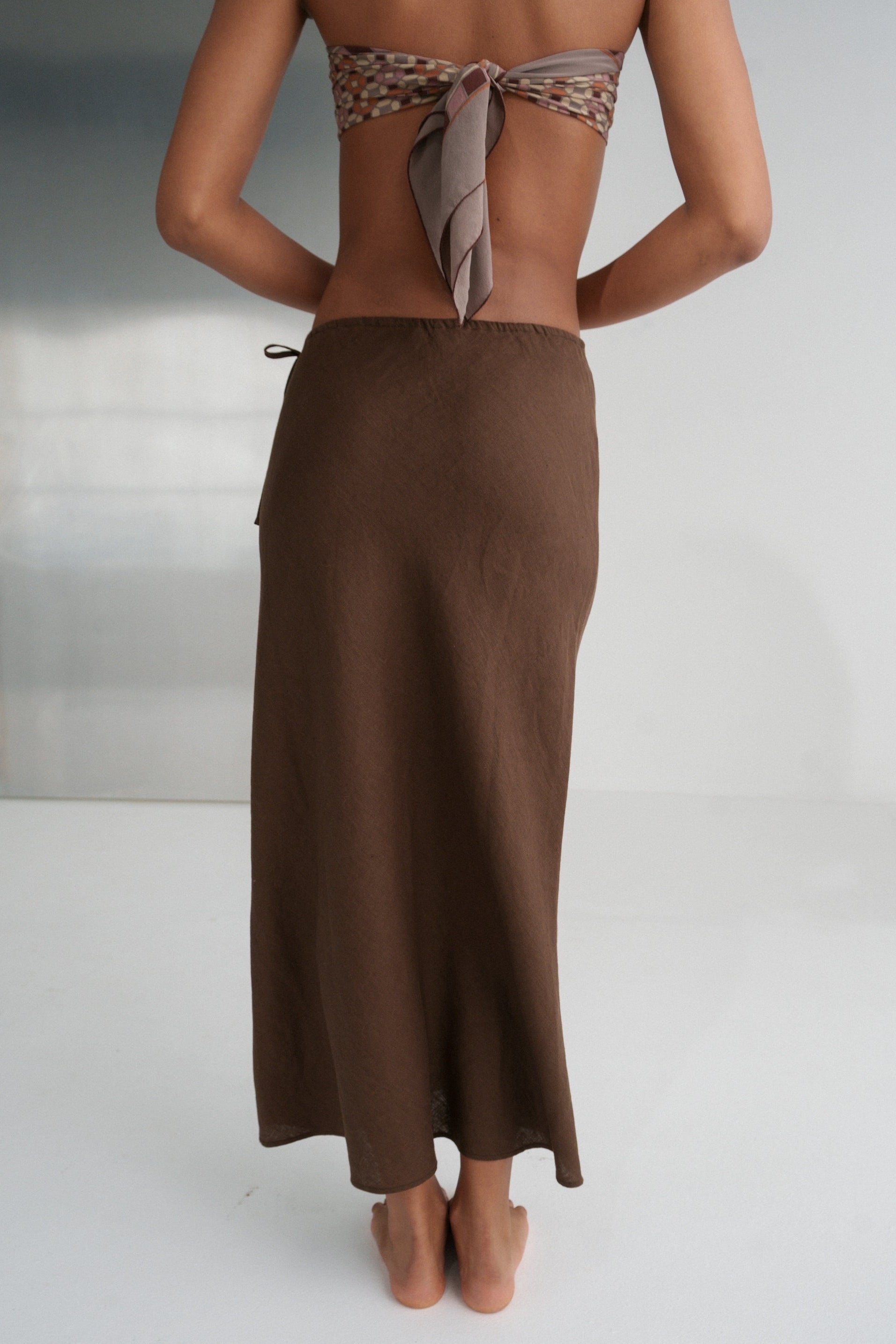 LILLY PILLY woman wearing Riley bias cut linen skirt in chocolate brown  on a white background, back view