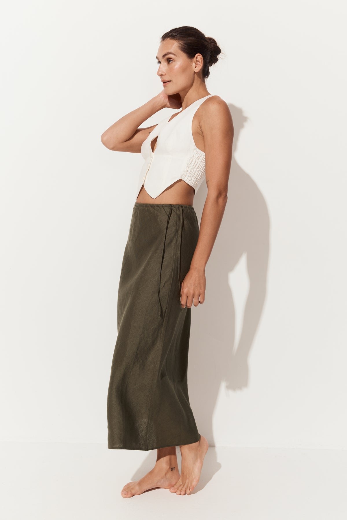 Riley Bias Linen Midi Skirt in Khaki - side view of woman wearing skirt paired with Ari linen ivory vest - Lilly Pilly Collection
