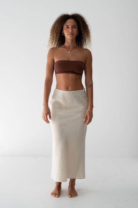 Riley Bias Linen Midi Skirt in Oatmeal - front view, bias-cut midi length, side tie detail, worn with chocolate bandeau top, gold jewellery - Lilly Pilly Collection