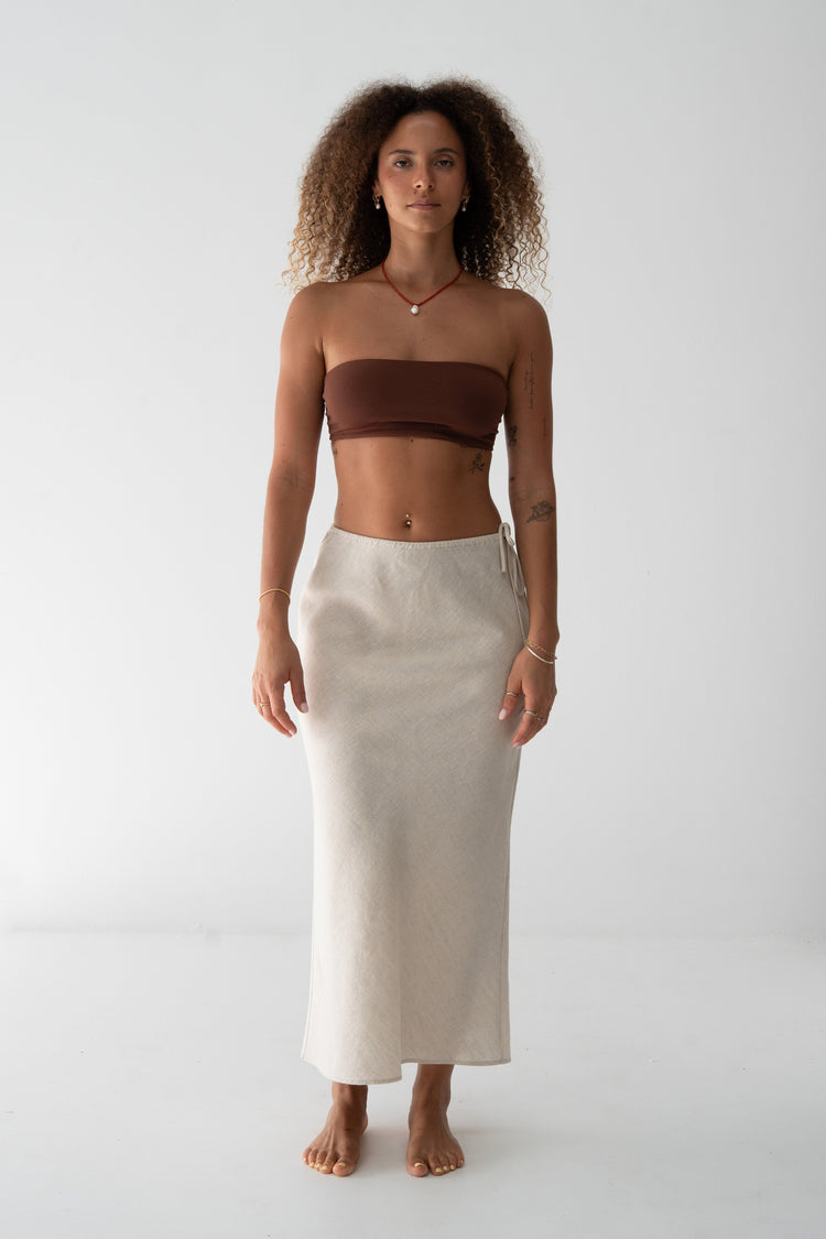 Riley Bias Linen Midi Skirt in Oatmeal - front view, bias-cut midi length, side tie detail, worn with chocolate bandeau top, gold jewellery - Lilly Pilly Collection