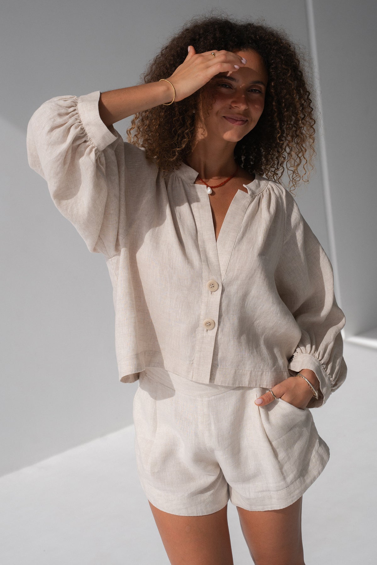 Rowan Linen Shirt in Oatmeal - hand shielding eyes, V-neckline and button-front, styled with matching linen shorts - Lilly Pilly Collection