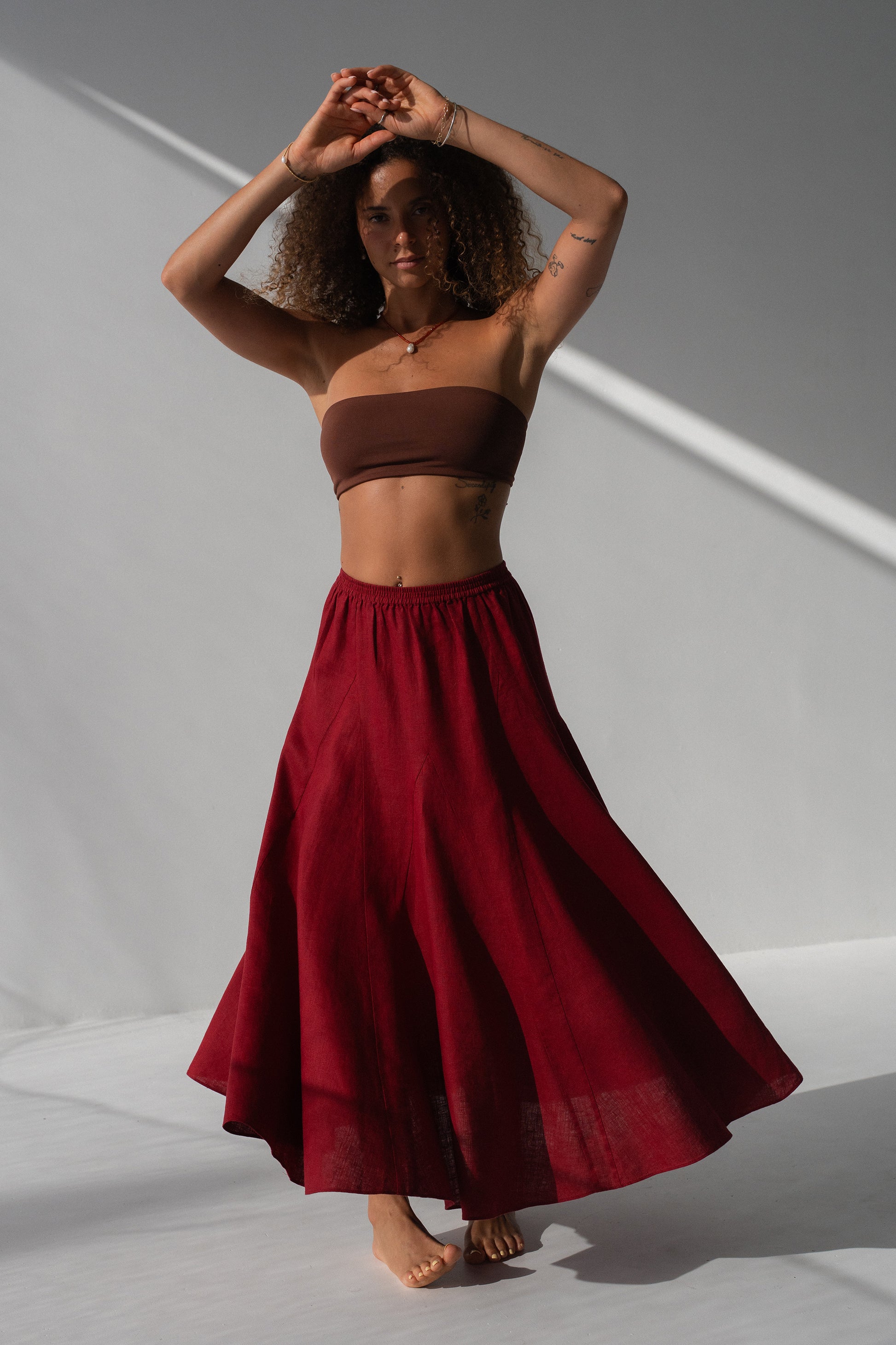 Stella Linen Maxi Skirt in Cherry Red - full length, woman wearing Cherry Red linen maxi skirt with brown bandeau top, skirt in motion, studio backdrop - Lilly Pilly Collection