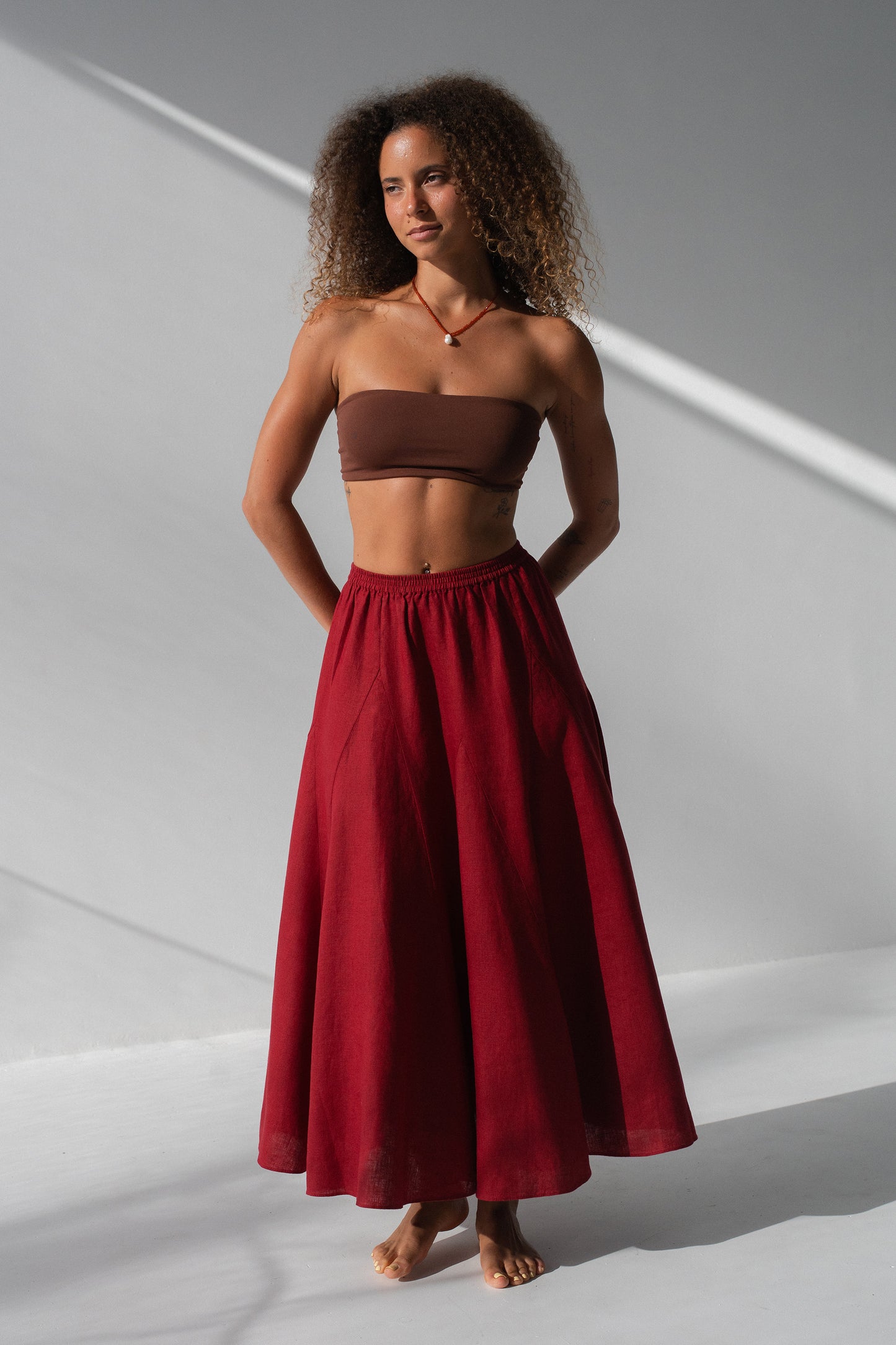 Stella Linen Maxi Skirt in Cherry Red - full length front view, woman wearing Cherry Red linen maxi skirt with brown bandeau top, studio backdrop - Lilly Pilly Collection