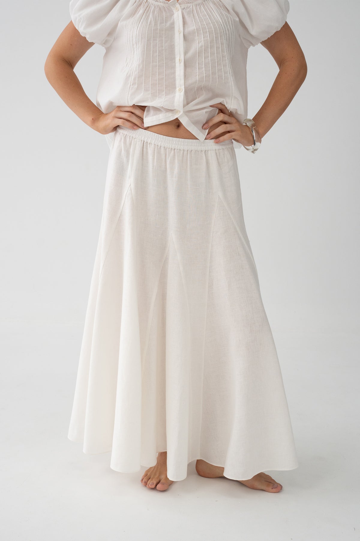 Stella Linen Maxi Skirt in Ivory - close-up of elasticated waistband and full A-line silhouette, woman wearing ivory pintuck crop top, studio backdrop - Lilly Pilly Collection