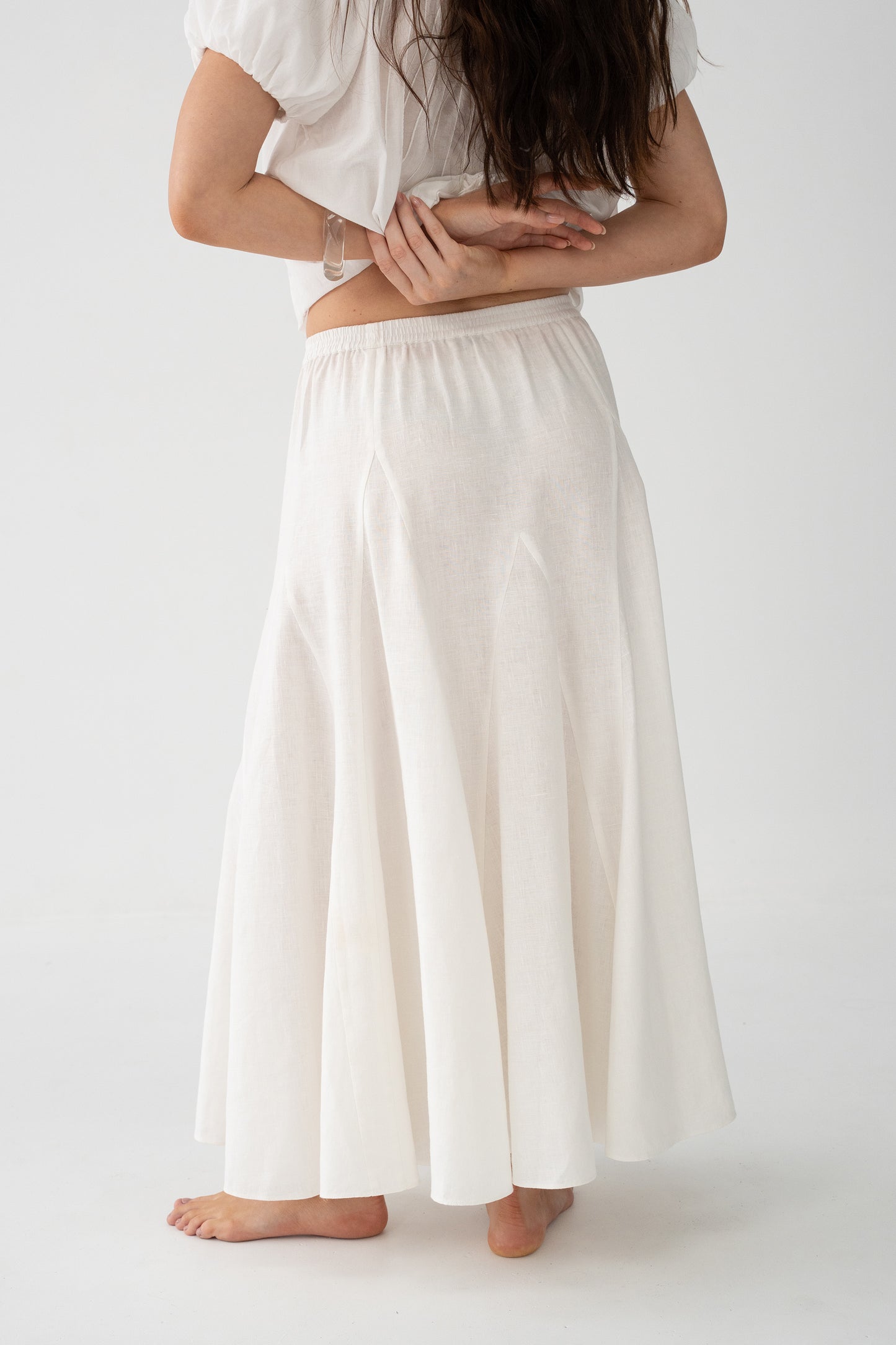 Stella Linen Maxi Skirt in Ivory - side view showing elasticated waistband and full A-line maxi silhouette, woman wearing matching ruffled crop top, studio backdrop - Lilly Pilly Collection