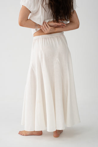 Stella Linen Maxi Skirt in Ivory - side view showing elasticated waistband and full A-line maxi silhouette, woman wearing matching ruffled crop top, studio backdrop - Lilly Pilly Collection