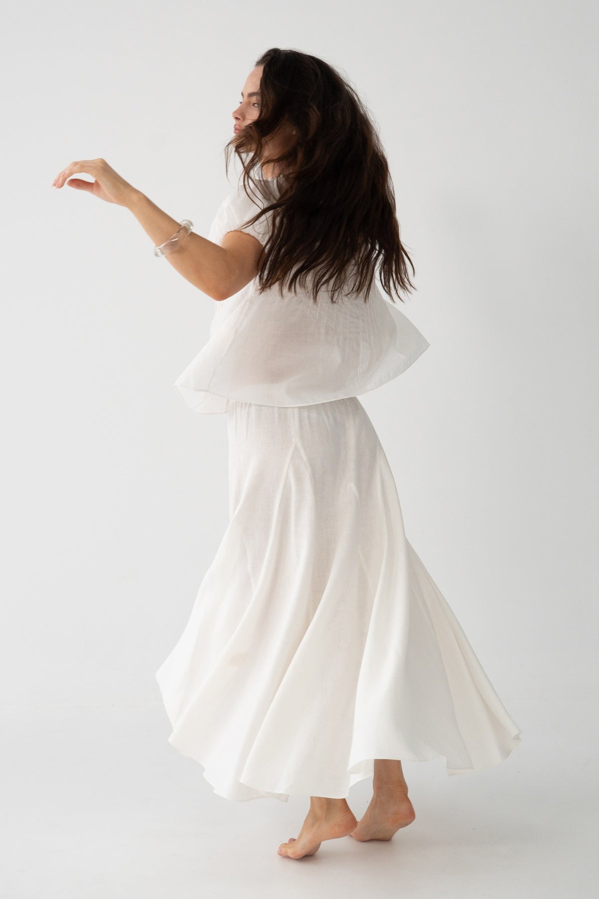Stella Linen Maxi Skirt in Ivory - side view, woman wearing Ivory linen skirt with matching ruffled crop top, full A-line silhouette in motion, studio backdrop - Lilly Pilly Collection