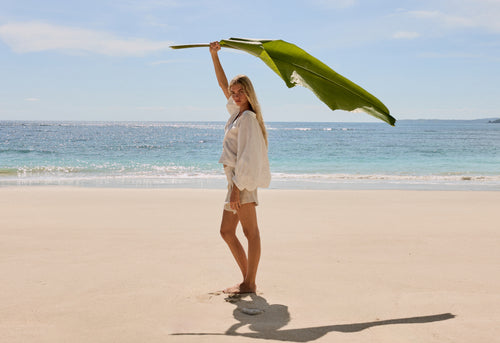 Rowan Linen Shirt in Ivory - side view standing on the beach shaded by palm leaf - Lilly Pilly Collection