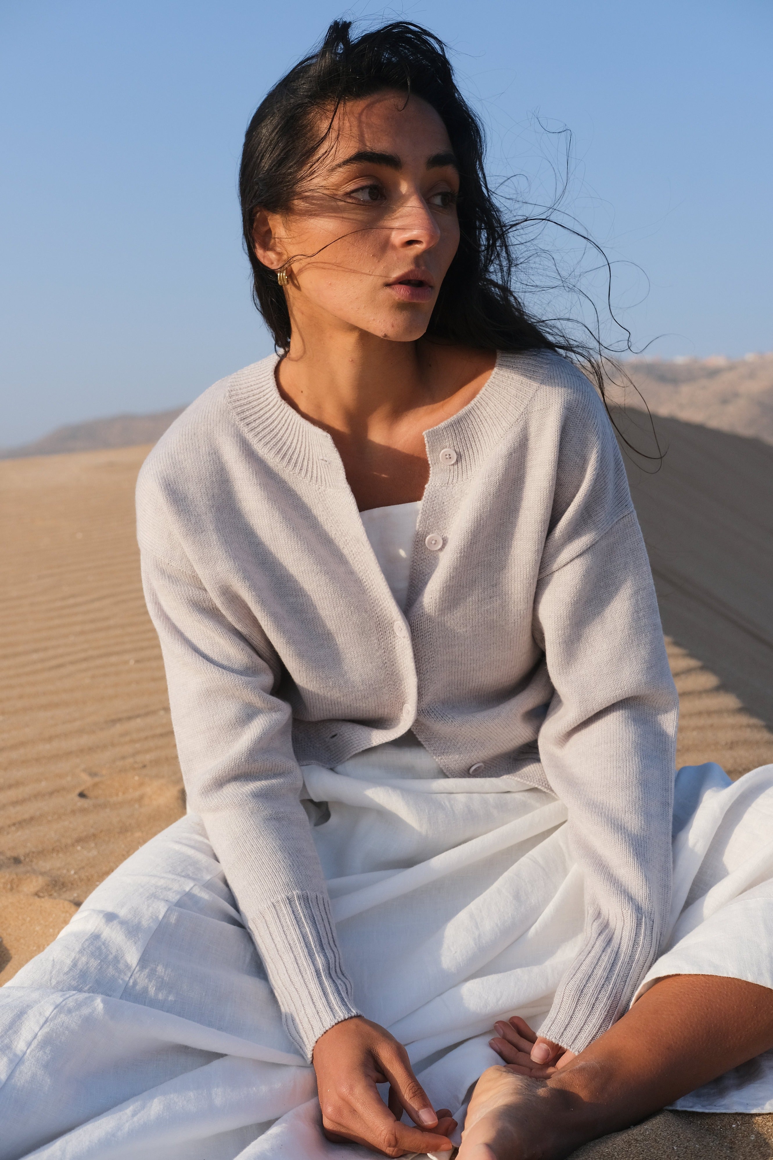 LILLY PILLY woman wearing fog coloured Taylor merino knit cardigan sitting in a desert landscape.