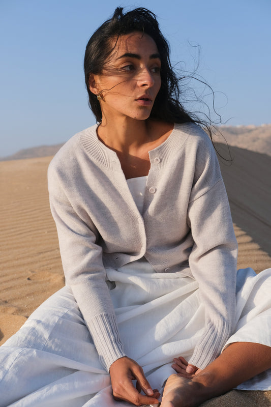 LILLY PILLY woman wearing fog coloured Taylor merino knit cardigan sitting in a desert landscape.