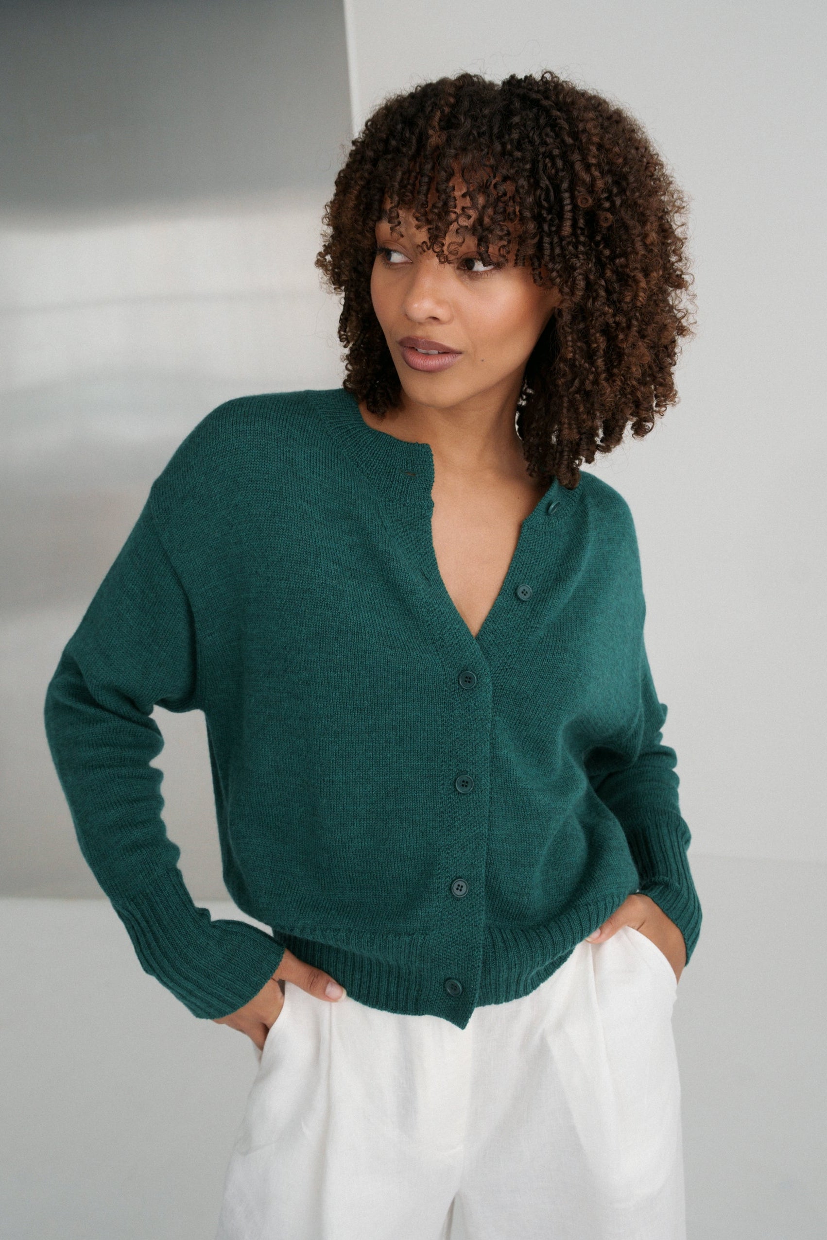 LILLY PILLY woman wearing pine green coloured Taylor merino knit cardigan  against a plain background